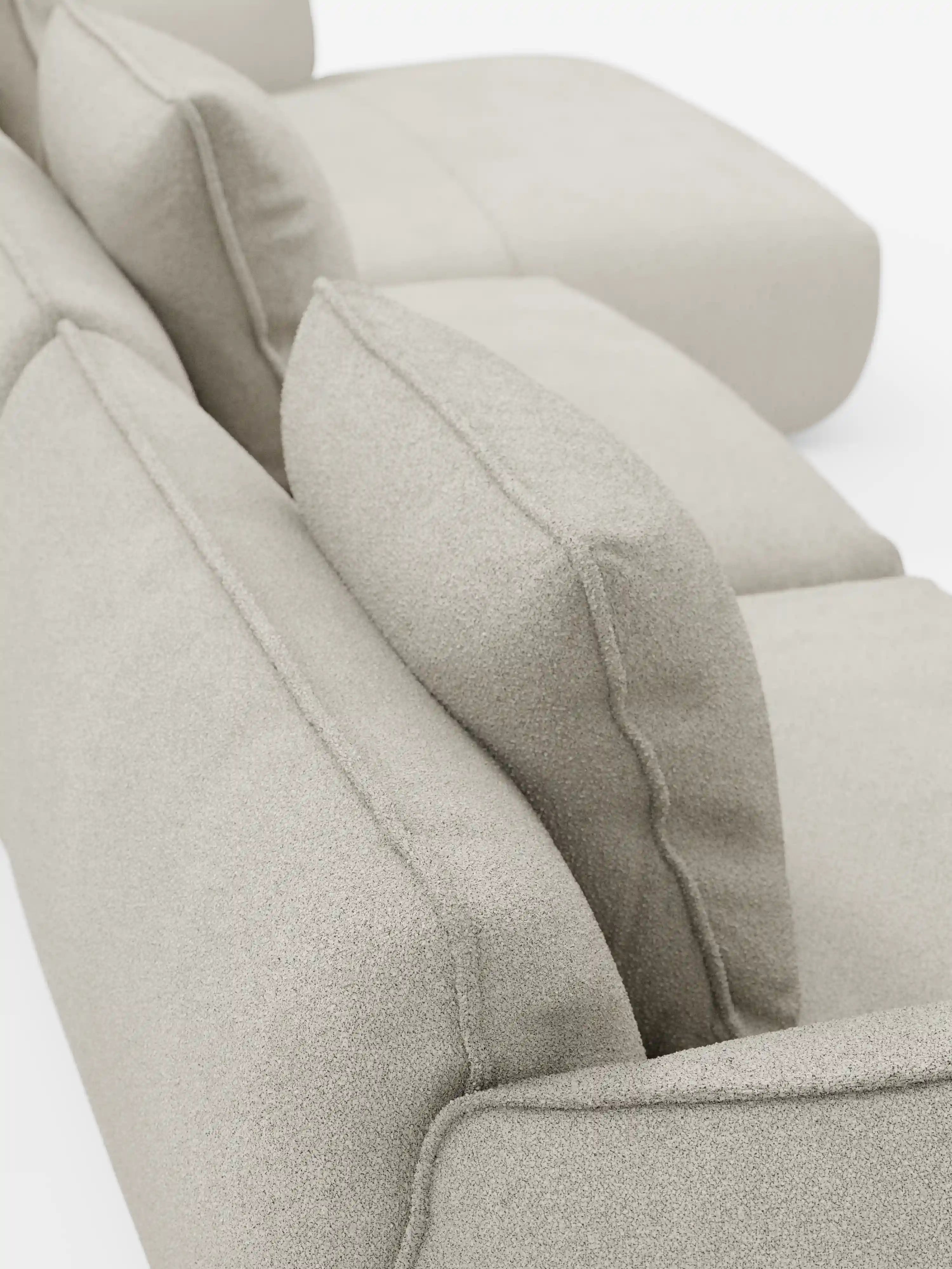Primo piano del divano angolare con penisola componibile Nimbus di Divani.Store, rivestito in morbido tessuto effetto cotone T33, resistente alle macchie, in una tonalità beige chiaro. L'immagine è ripresa da dietro e leggermente dall'alto, mettendo in risalto i cuscini morbidi e testurizzati e mostrando l'allineamento dello schienale e della seduta su uno sfondo bianco.