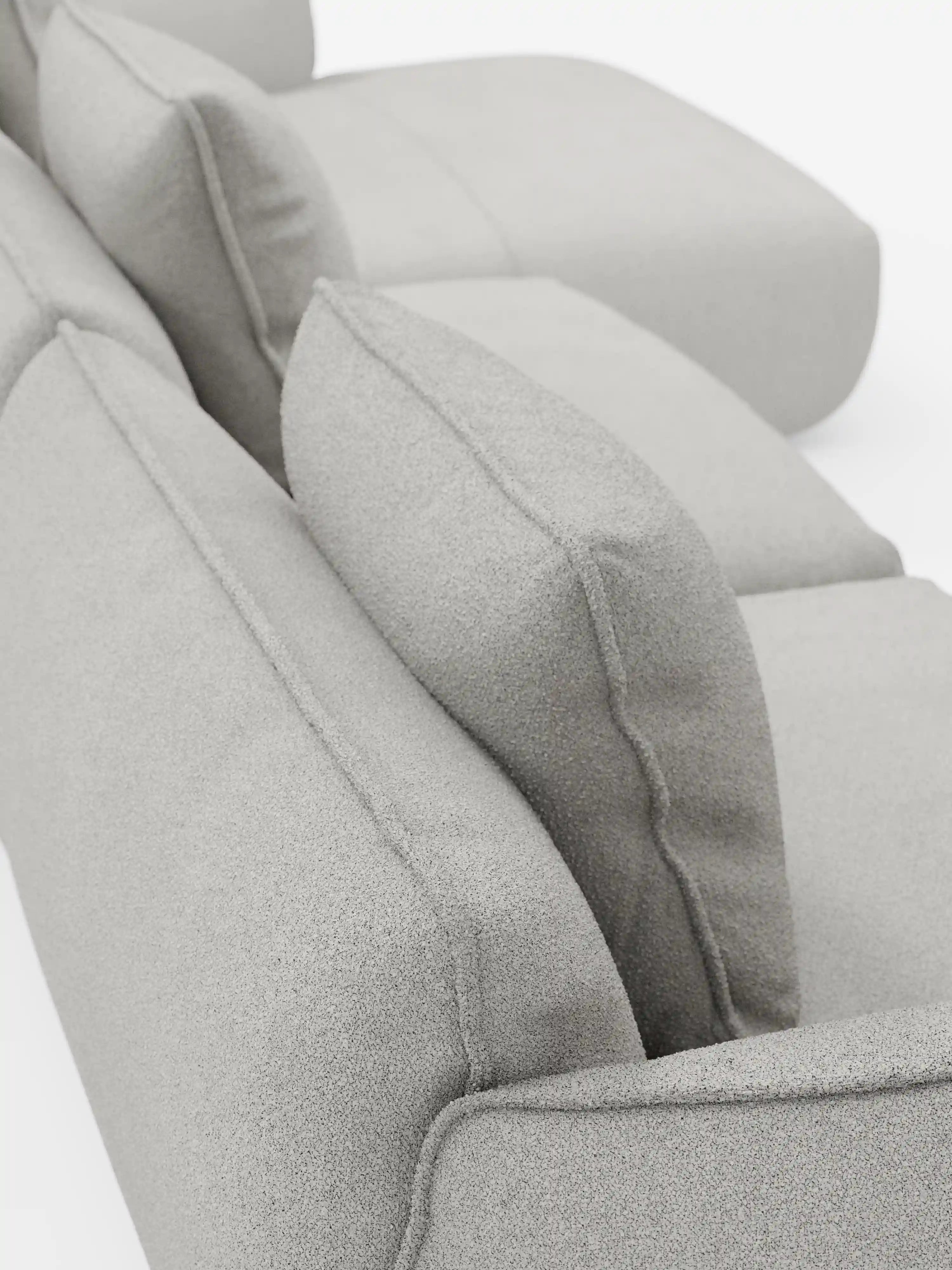 Primo piano del divano angolare con penisola componibile Nimbus in morbido tessuto effetto cotone antimacchia T33 di Divani.Store, che mette in risalto il suo tessuto grigio chiaro morbido effetto cotone antimacchia, i soffici cuscini dello schienale con bordature a filetto e i braccioli arrotondati su uno sfondo bianco.