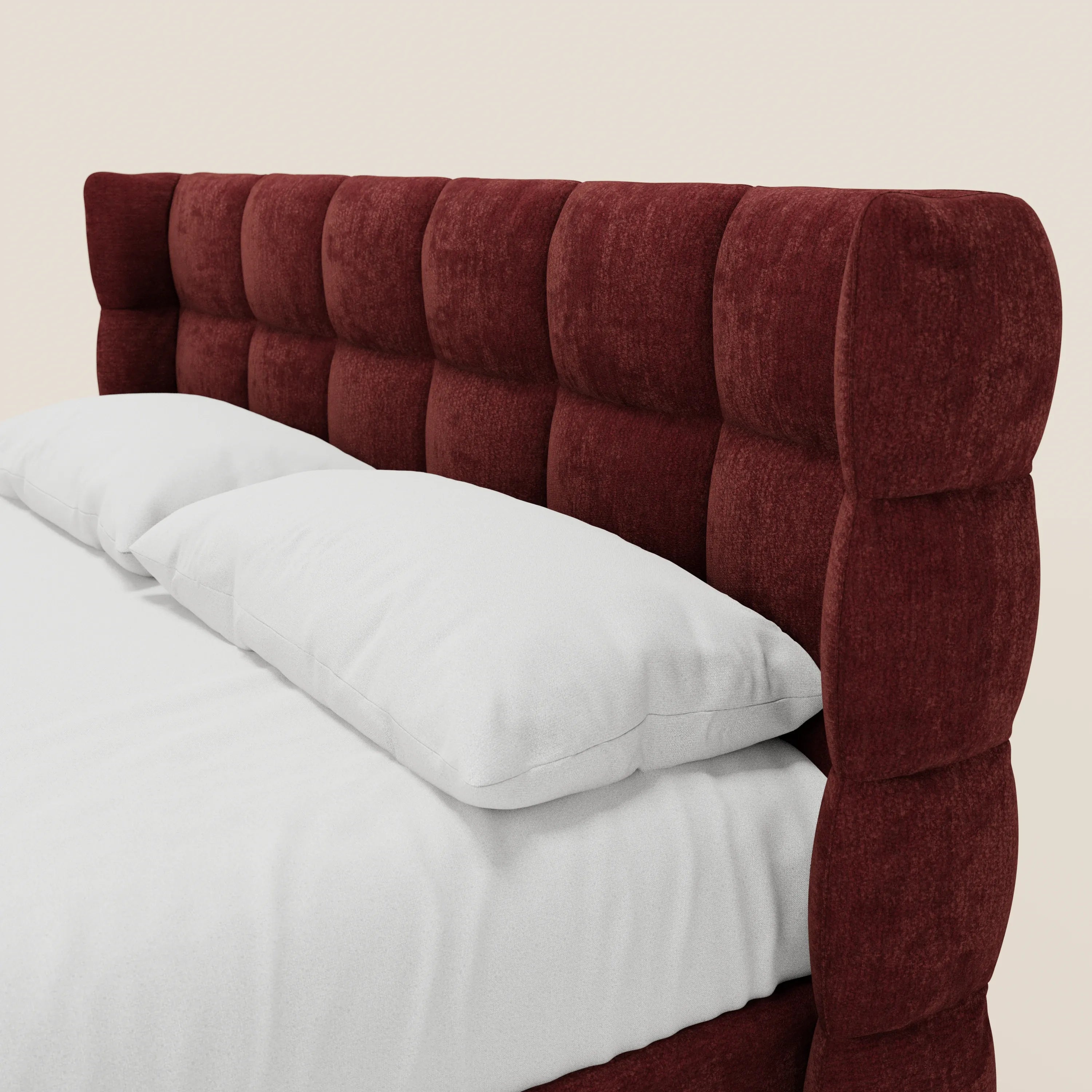 Un primo piano del letto imbottito RAGNAR con vano contenitore e testiera capitonné avvolgente di Letti.store, realizzato in morbido tessuto marrone rossiccio certificato Oeko-Tex®, con sezioni imbottite quadrate sopra la biancheria da letto candida e due cuscini.
