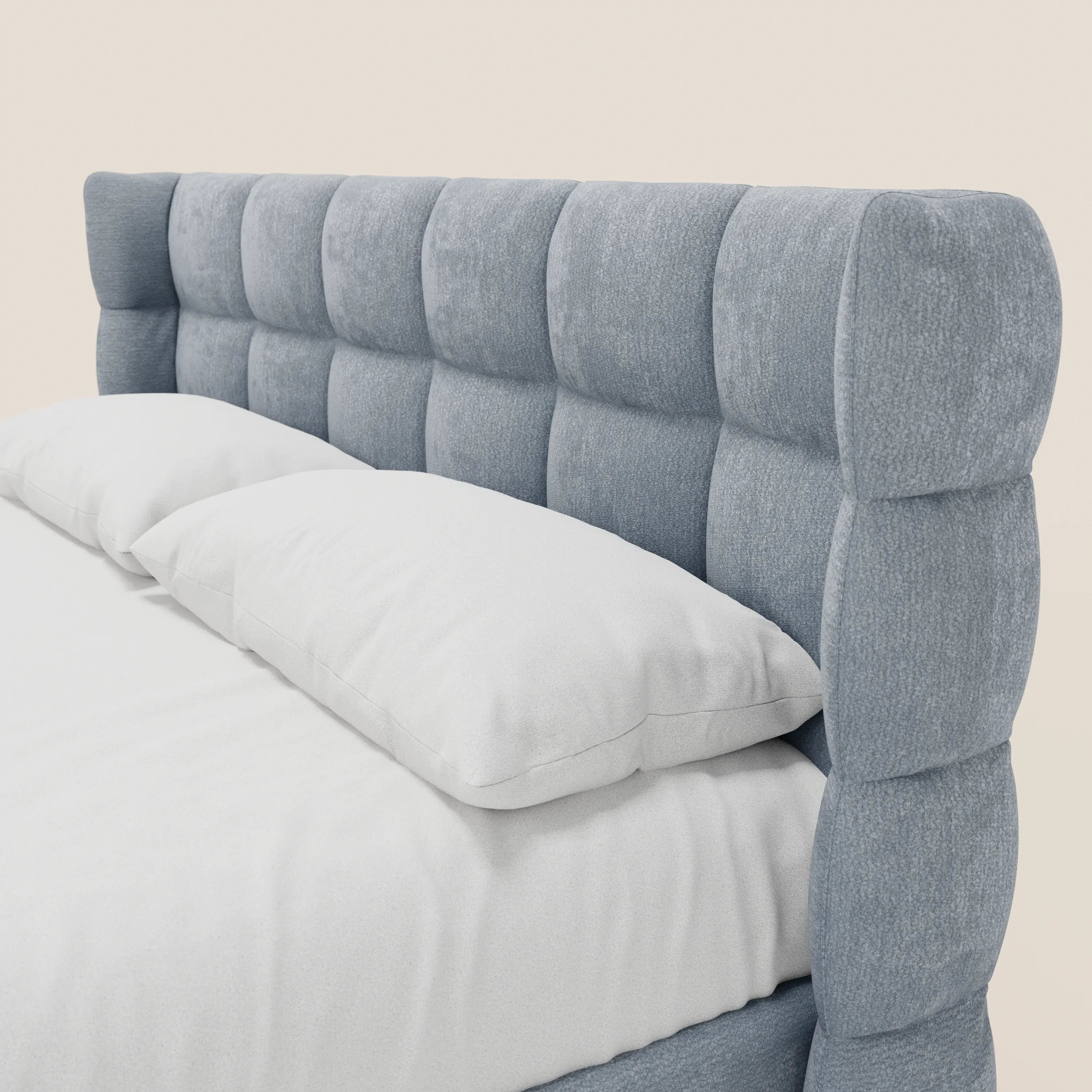 Primo piano del letto imbottito RAGNAR con contenitore e testiera capitonné avvolgente in tessuto azzurro certificato Oeko-Tex® di Letti.store, con biancheria da letto bianca e due cuscini su uno sfondo chiaro e uniforme.