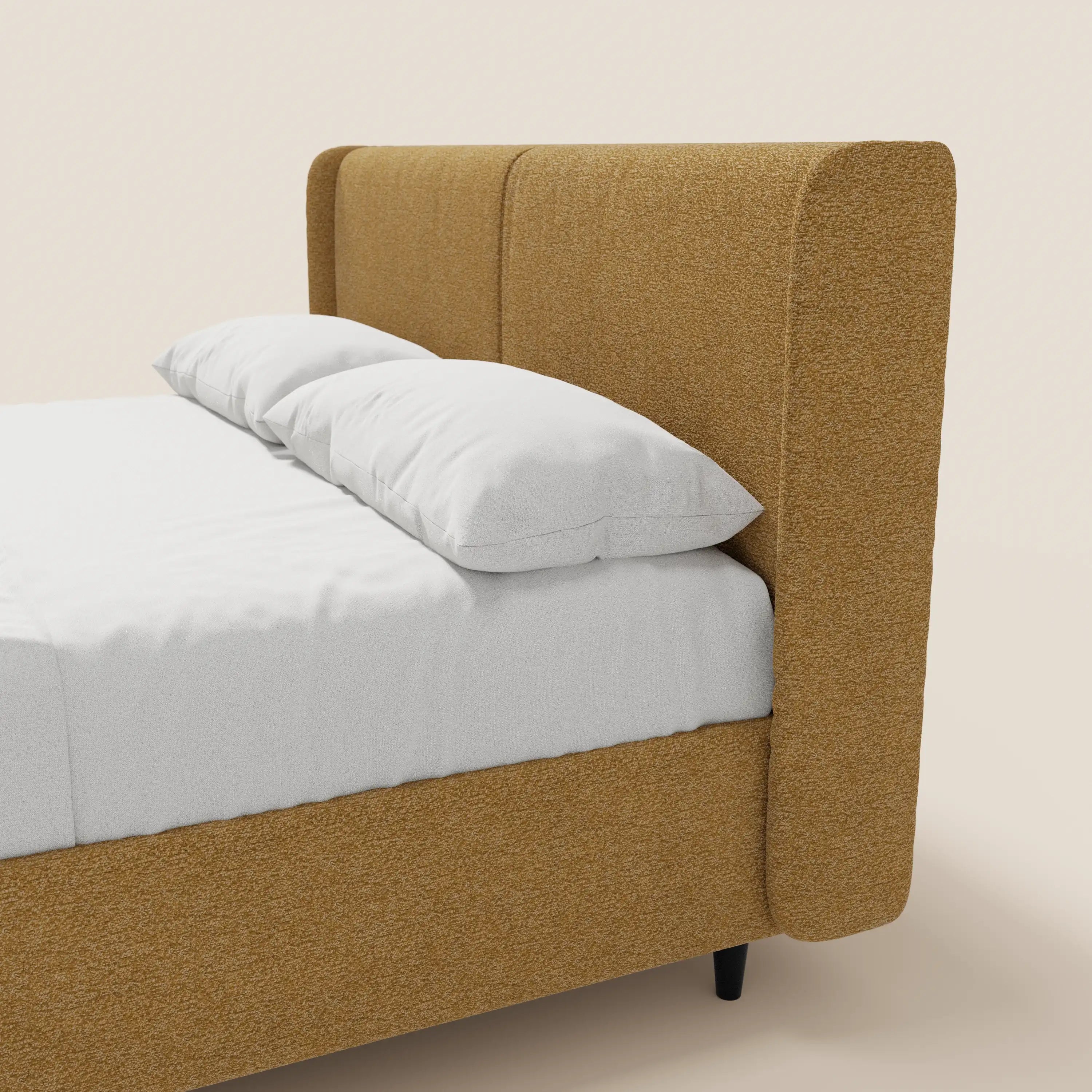VALKIRIA di Letti.store: letto di design con contenitore, testiera avvolgente e 2 cuscini imbottiti in tessuto Oeko-Tex®. Moderno letto imbottito color senape dalle linee pulite e con gambe nere affusolate, completato da lenzuola e cuscini bianchi.