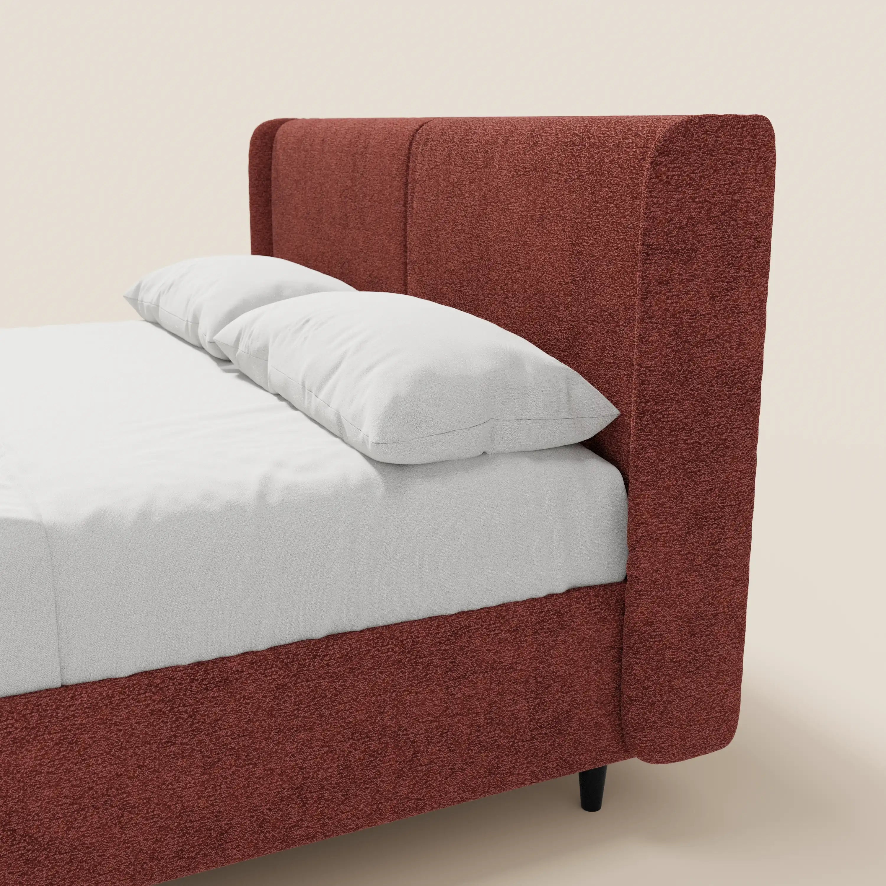 Viene mostrata la metà sinistra del letto di design VALKIRIA di Letti.store, caratterizzato da un rivestimento con finitura ruggine certificato Oeko-Tex®, una testiera alta imbottita con 2 cuscini imbottiti, un materasso bianco e uno sfondo beige chiaro. Include un vano portaoggetti.