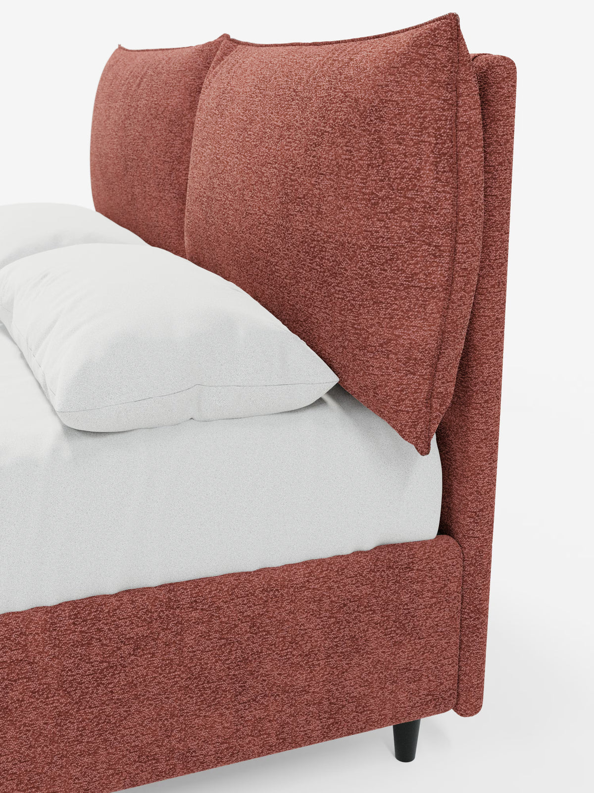 Primo piano del letto imbottito ZAYRON con contenitore e morbidi cuscini regolabili di Letti.store, caratterizzato da una struttura imbottita color bruno-rossastro in tessuto certificato Oeko-Tex® e da due grandi cuscini angolari e soffici che fungono da testata morbida e regolabile. Il materasso è coperto da un lenzuolo con angoli bianco, mentre il letto poggia su corte gambe nere su uno sfondo bianco a tinta unita.
