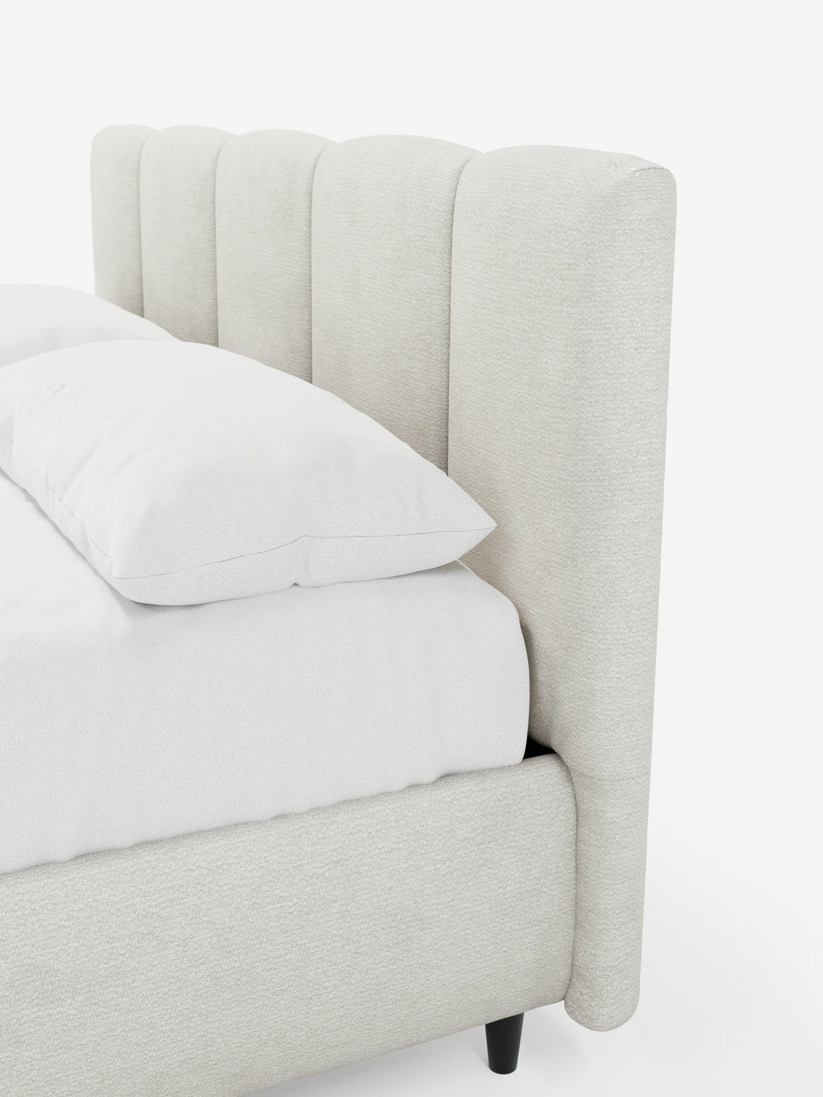 Un primo piano del letto imbottito ARKAM con contenitore e testiera a lavorazione verticale di Letti.store, caratterizzato da una testiera alta e imbottita con scanalature verticali, rivestita in tessuto beige chiaro certificato Oeko-Tex®. La biancheria da letto e i cuscini sono bianchi, mentre la gamba visibile del letto è corta e nera. Lo sfondo è bianco a tinta unita.