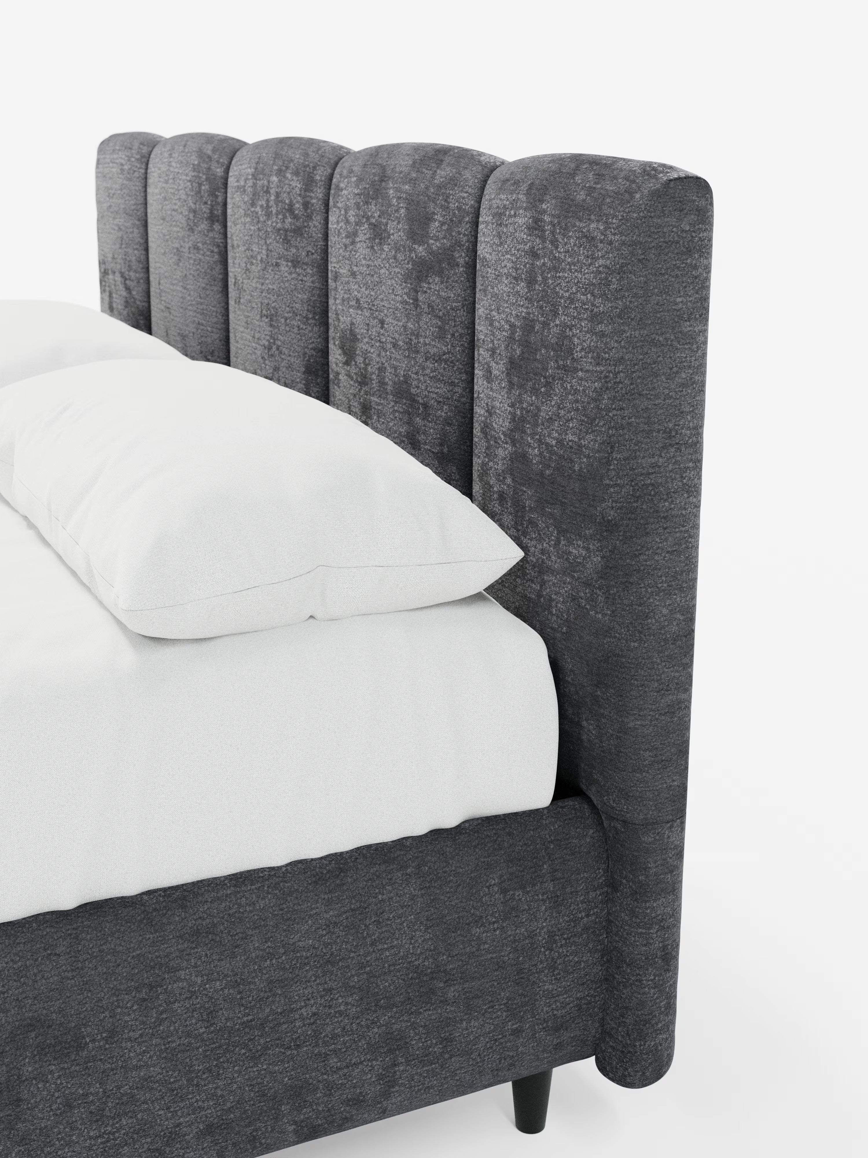 Una vista angolare del letto imbottito ARKAM con contenitore e testiera a lavorazione verticale di Letti.store, che mette in risalto la sua testiera alta e morbida, con dettagli verticali in tessuto certificato Oeko-Tex®. La struttura imbottita abbinata è rivestita con biancheria da letto di un bianco candido e due grandi cuscini bianchi, il tutto su uno sfondo bianco a tinta unita per esaltarne il design shabby chic.