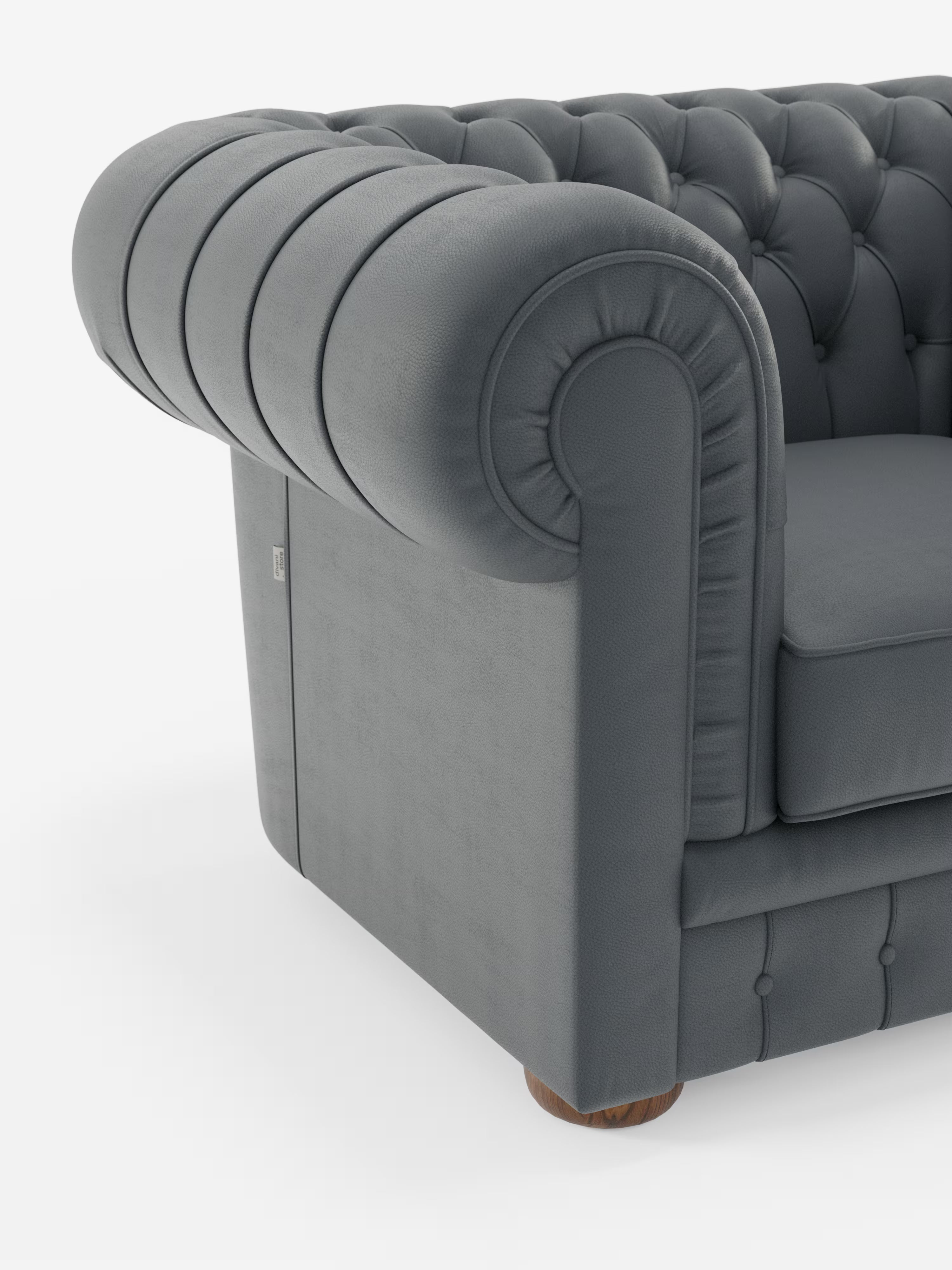 Primo piano di una poltrona Chester in vera pelle spessorata con capitonné artigianale di Divani.Il modello, caratterizzato da una finitura in vera pelle grigio scuro, ampi braccioli arrotondati con pieghe decorative, capitonné profondo realizzato a mano in classico stile Chester e un unico piede in legno a vista alla base, è presentato su uno sfondo bianco a tinta unita.