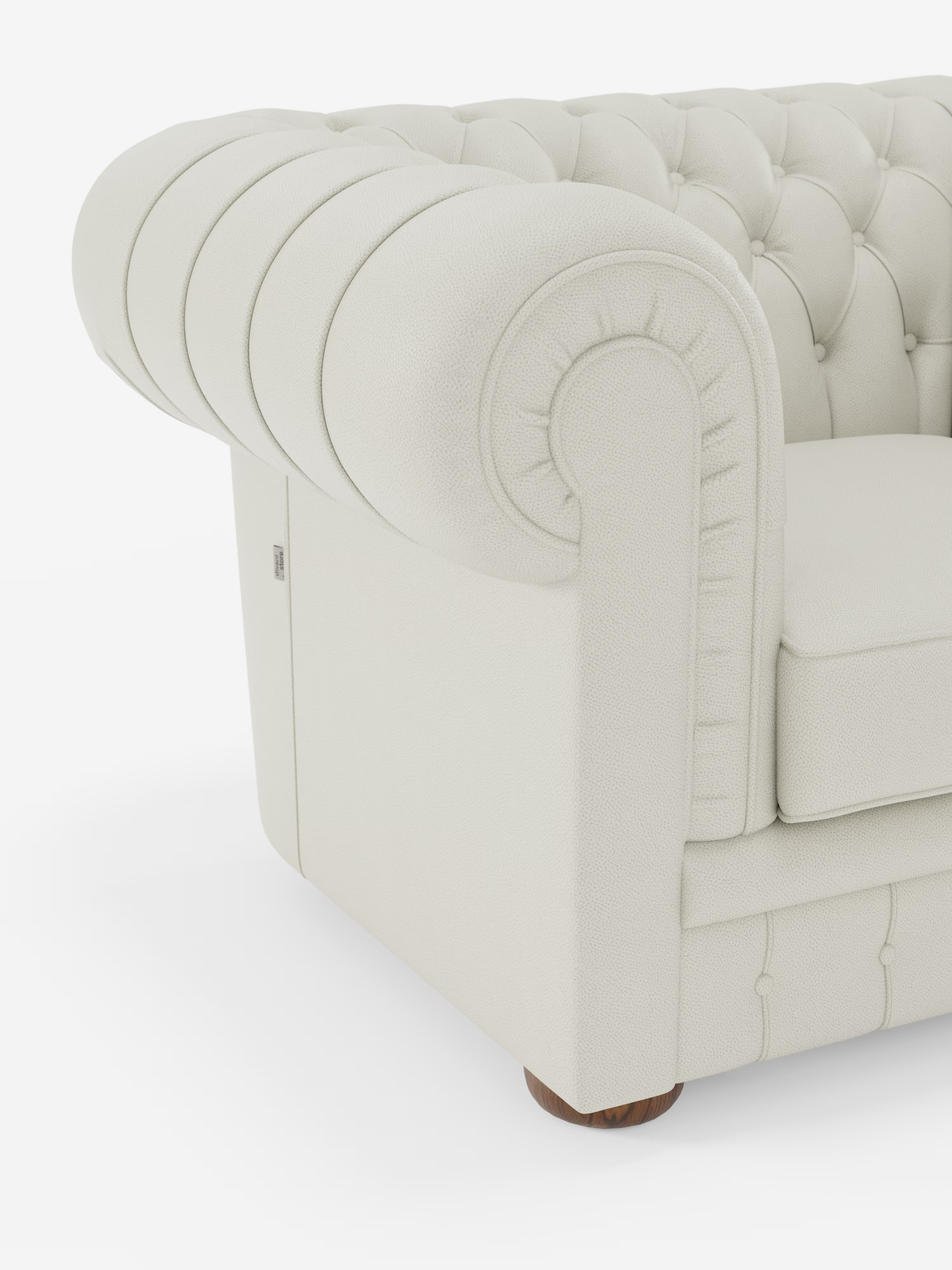 Primo piano della poltrona Chester in vera pelle spessorata con capitonné artigianale di Divani.Store, che mette in risalto un lussuoso angolo color crema che richiama il classico design delle poltrone capitonné. Il bracciolo è di dimensioni generose, arrotondato e presenta profondi bottoni trapuntati a mano con rivestimento in vera pelle testurizzata. Sotto il divano è visibile una gamba in legno, il tutto su uno sfondo bianco a tinta unita.