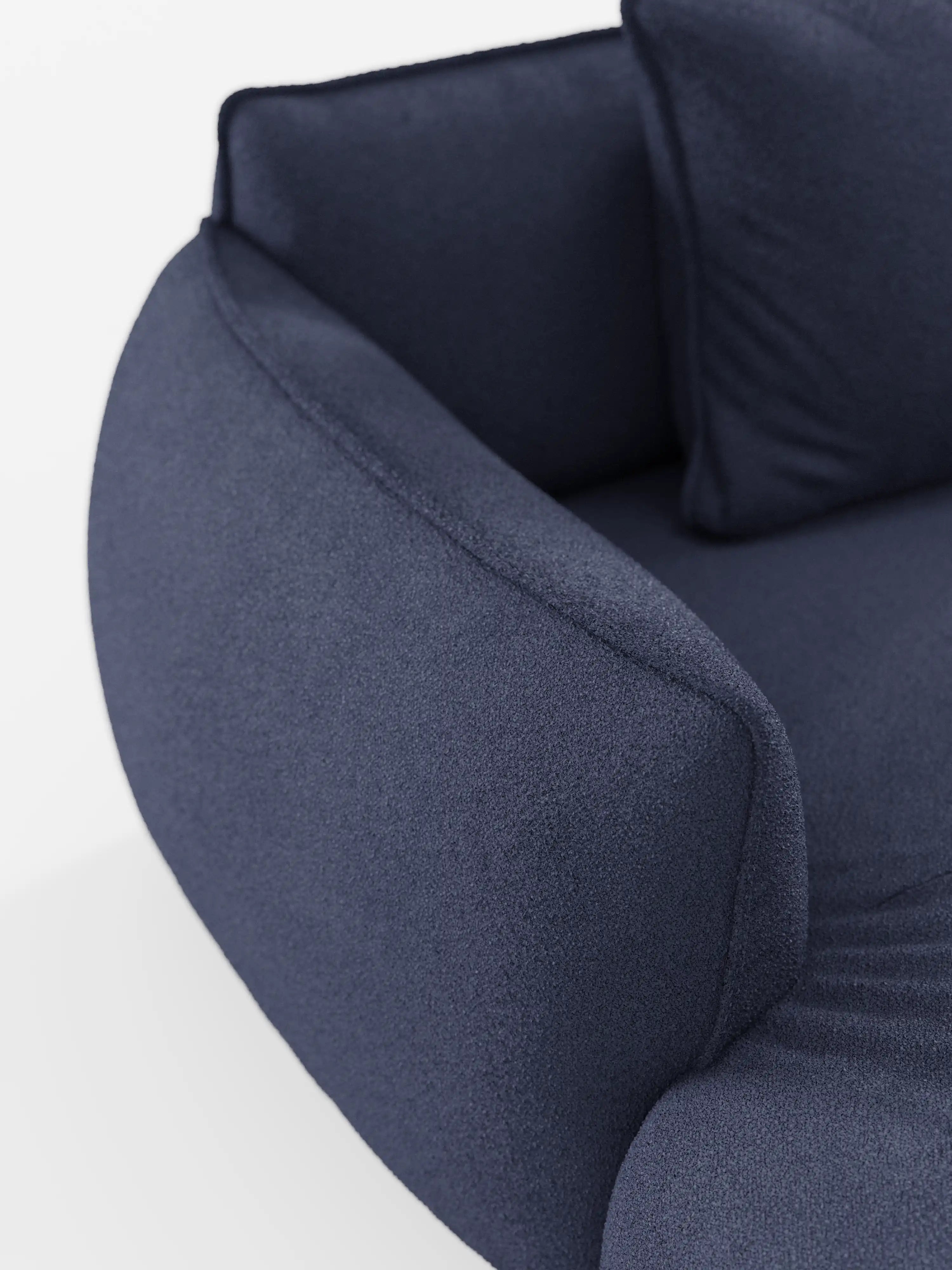 Primo piano del divano angolare modulare panoramico Nimbus con penisola e design angolare, rivestito in tessuto t33 blu intenso resistente alle macchie, caratterizzato da braccioli curvi e da un cuscino coordinato. Presentato su uno sfondo bianco a tinta unita, il materiale morbido e materico mette in risalto la raffinata maestria artigianale che contraddistingue i mobili Made in Italy di Divani.Store.