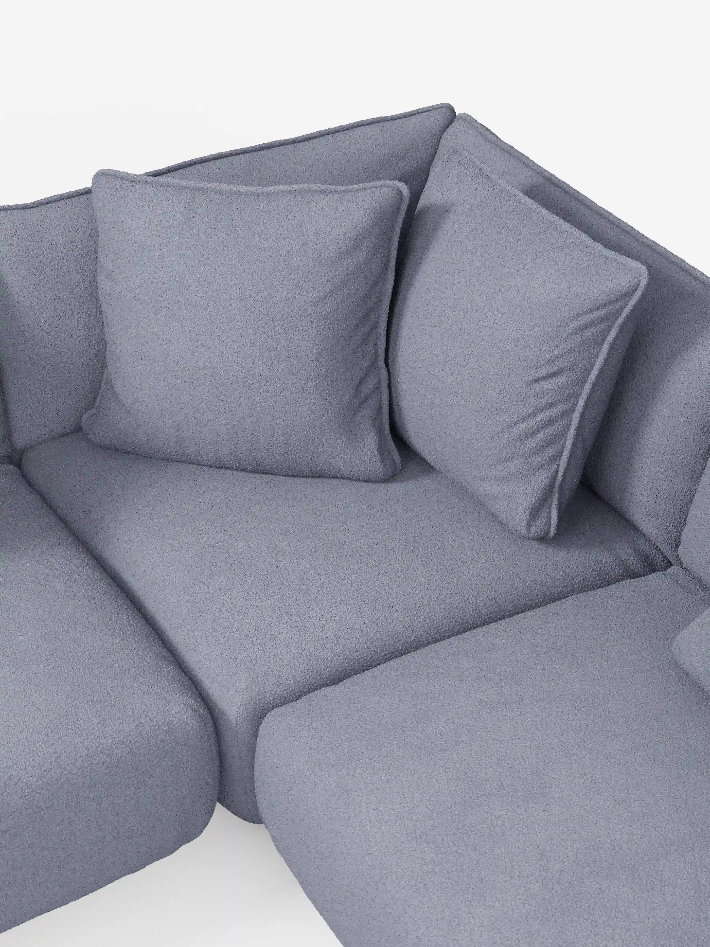 Un primo piano del divano angolare panoramico componibile Nimbus con penisola e angolo in tessuto smacchiabile T33 di Divani.Store ne mette in risalto il moderno rivestimento grigio. Due grandi cuscini quadrati poggiano contro lo schienale angolato, sottolineando l’accogliente design a forma di L su uno sfondo chiaro ed evidenziandone il comfort e la semplicità.