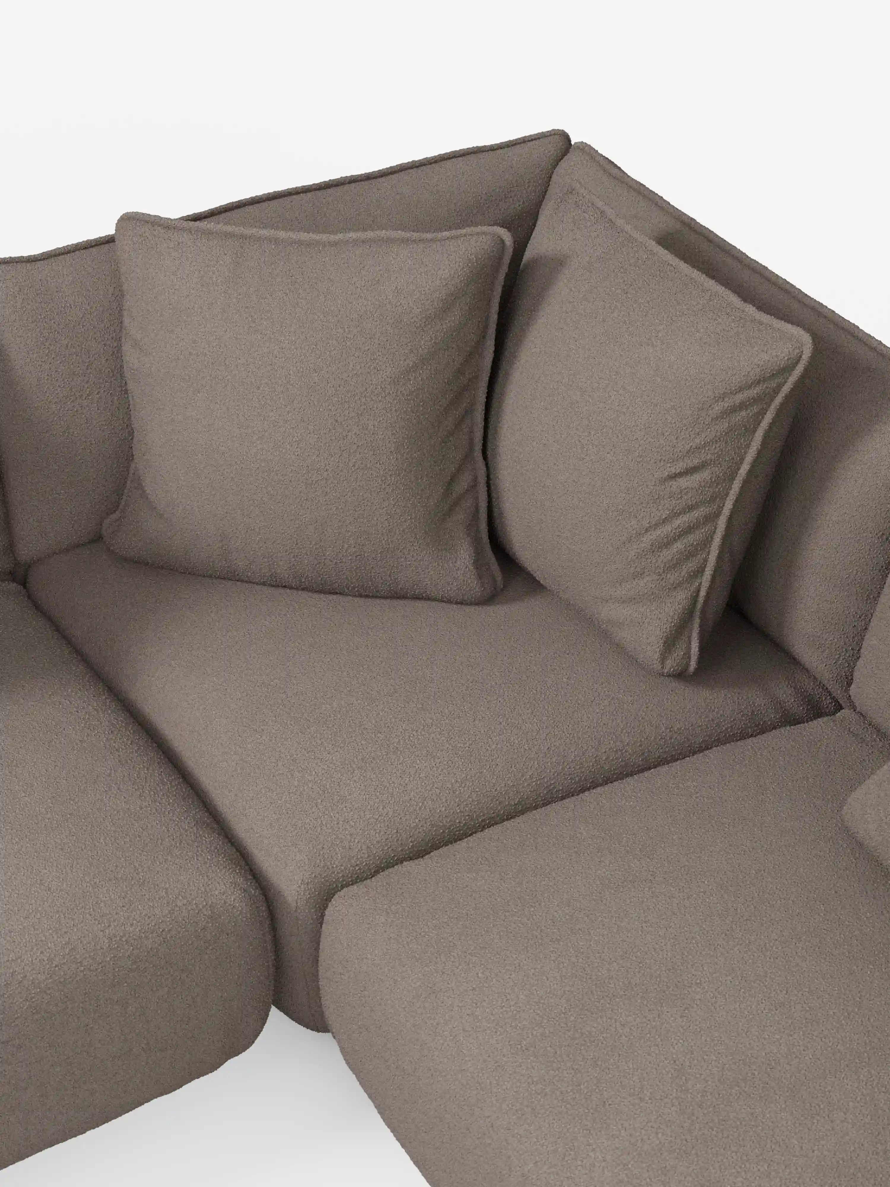 Un primo piano dell'angolo del divano angolare panoramico componibile Nimbus con penisola e angolo in tessuto antimacchia T33 di Divani.Store, caratterizzato da un morbido rivestimento in tessuto color taupe antimacchia e da due cuscini quadrati per lo schienale. Questo divano componibile Made in Italy si distingue per le linee pulite e arrotondate e l’aspetto confortevole, che risalta sullo sfondo bianco chiaro e uniforme.