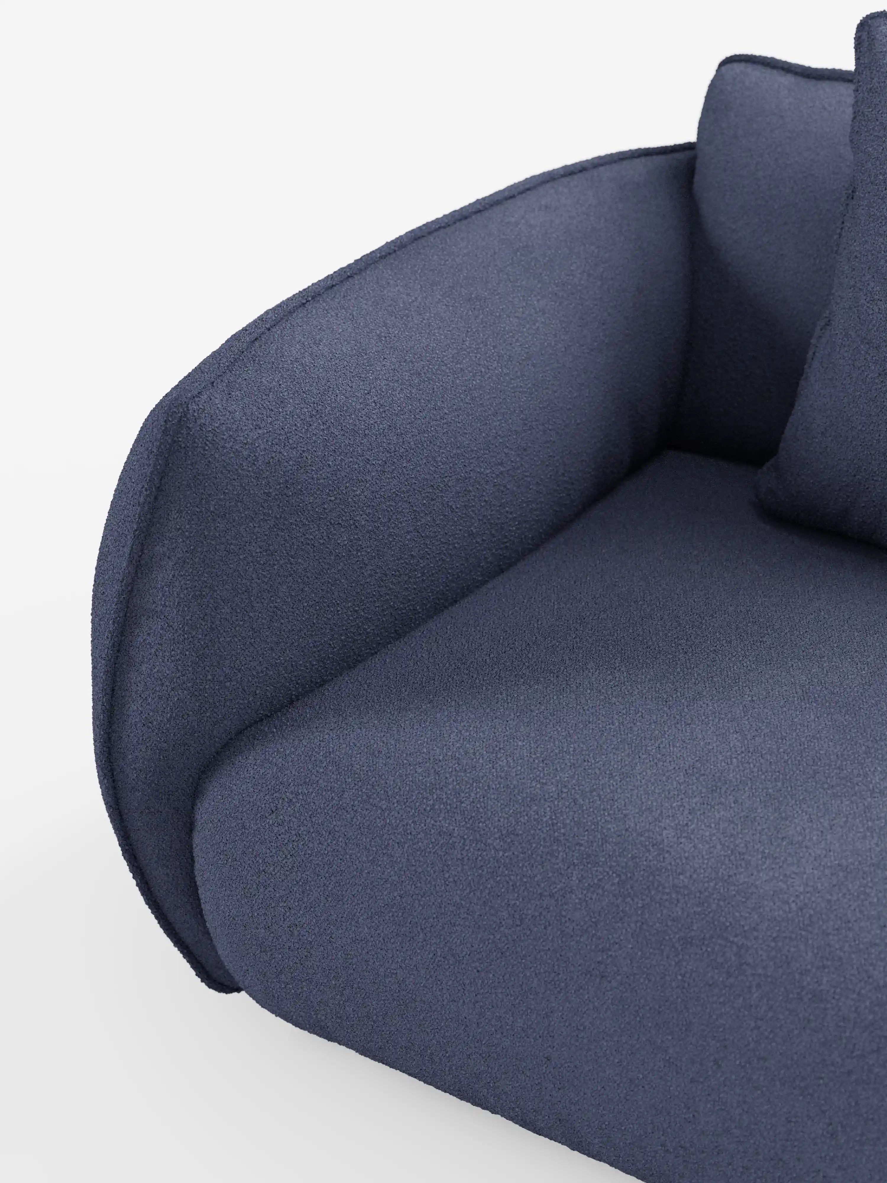 Primo piano del divano angolare con penisola componibile Nimbus di Divani.Store, rivestito in tessuto T33 blu scuro, con effetto cotone e texture, resistente alle macchie. I braccioli arrotondati e il cuscino di seduta ne sottolineano la morbida imbottitura, mentre un cuscino coordinato è parzialmente visibile nell’angolo in alto a destra su uno sfondo bianco a tinta unita, mettendo in risalto il design moderno di questo divano contemporaneo.