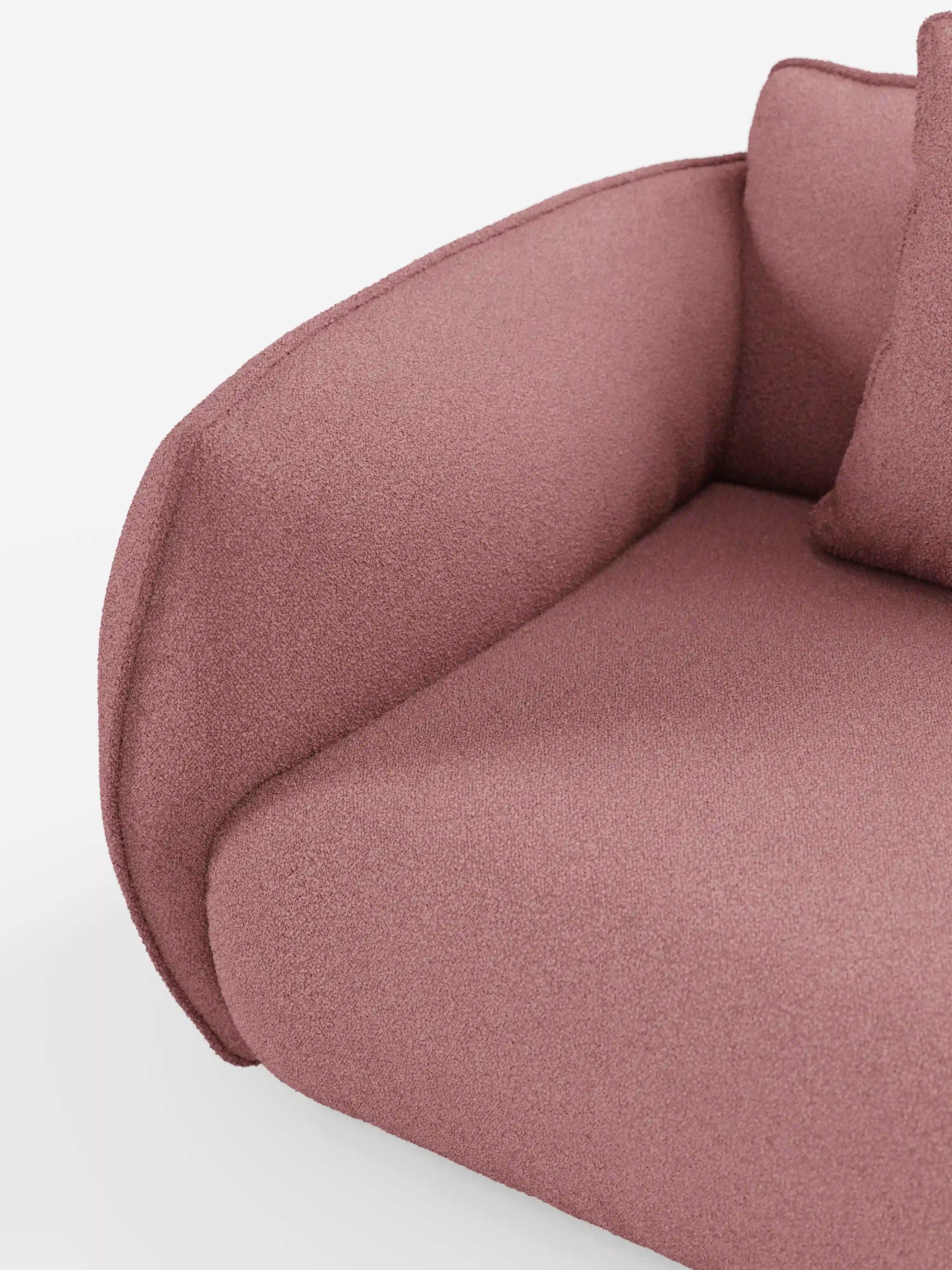 Primo piano del divano angolare con penisola componibile Nimbus di Divani.Store, in un delicato rosa, realizzato in morbido tessuto T33 effetto cotone e resistente alle macchie. Il bracciolo presenta bordi lisci e arrotondati che ne sottolineano l'elegante design moderno. Il rivestimento testurizzato e un cuscino abbinato risaltano su uno sfondo bianco a tinta unita.