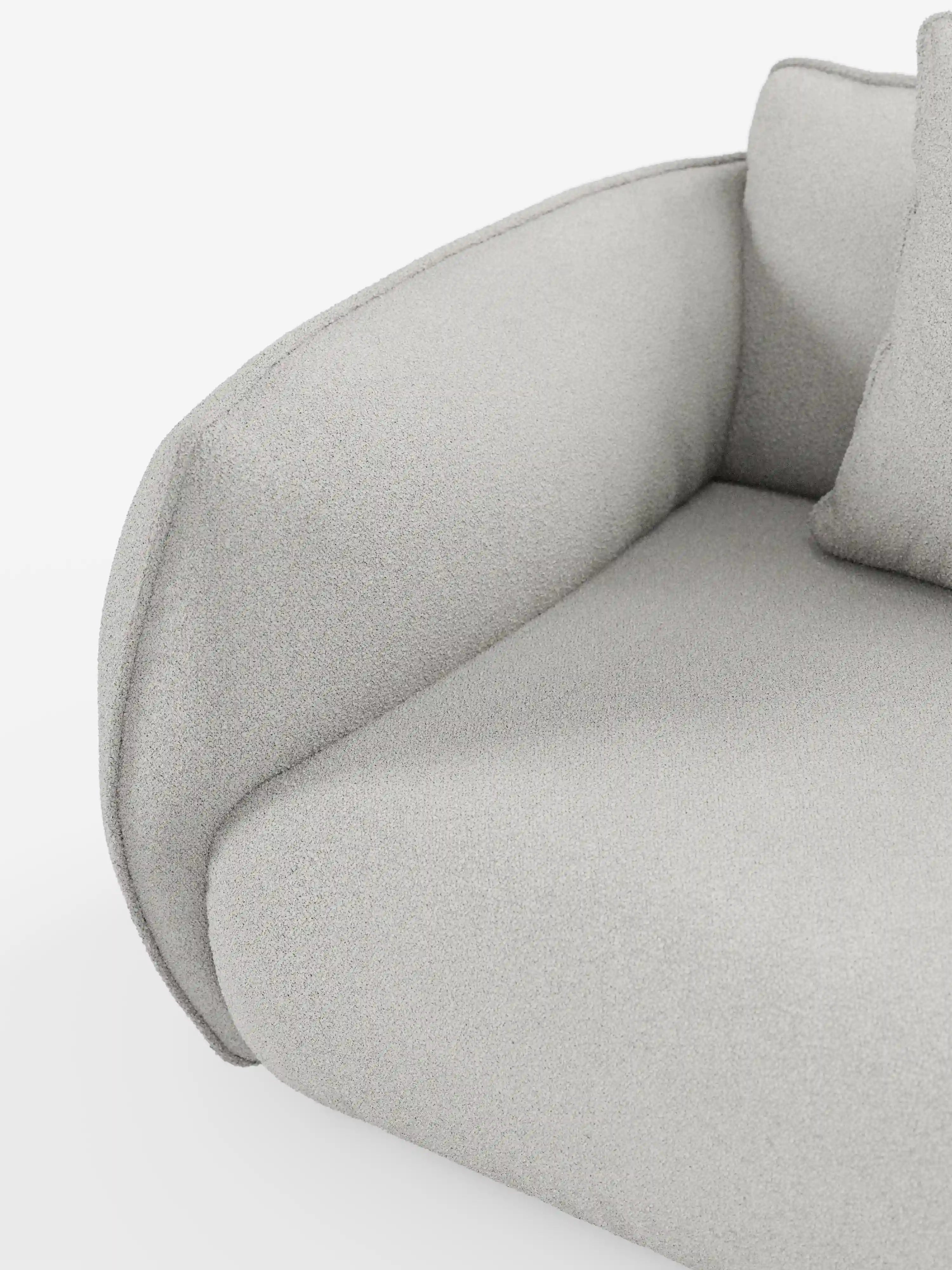 Primo piano del divano angolare con penisola componibile Nimbus di Divani.Store, rivestito in tessuto T33 grigio chiaro, morbido, dall’effetto cotone e resistente alle macchie. L'immagine mostra il bracciolo ricurvo di questo divano moderno, il cuscino spesso e un set di cuscini coordinati su uno sfondo bianco, mettendo in risalto la trama morbida e leggermente felpata che garantisce un comfort eccezionale.