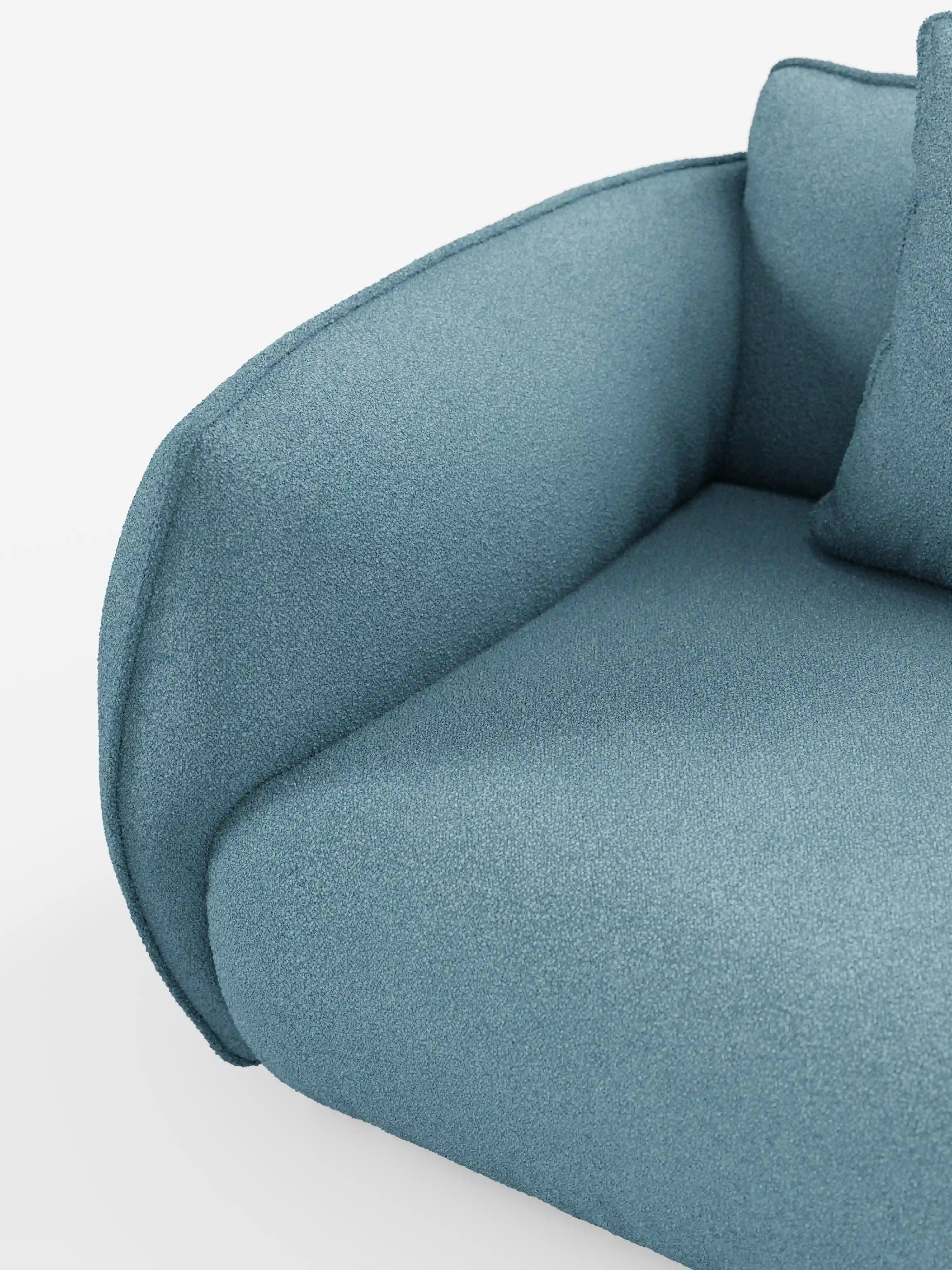 Un primo piano del divano angolare con penisola componibile Nimbus di Divani.Store, rivestito in morbido tessuto T33 blu con effetto cotone, resistente alle macchie. L'immagine mette in risalto il bracciolo, che si fonde armoniosamente con la seduta e lo schienale, con un cuscino blu coordinato parzialmente visibile su uno sfondo bianco.