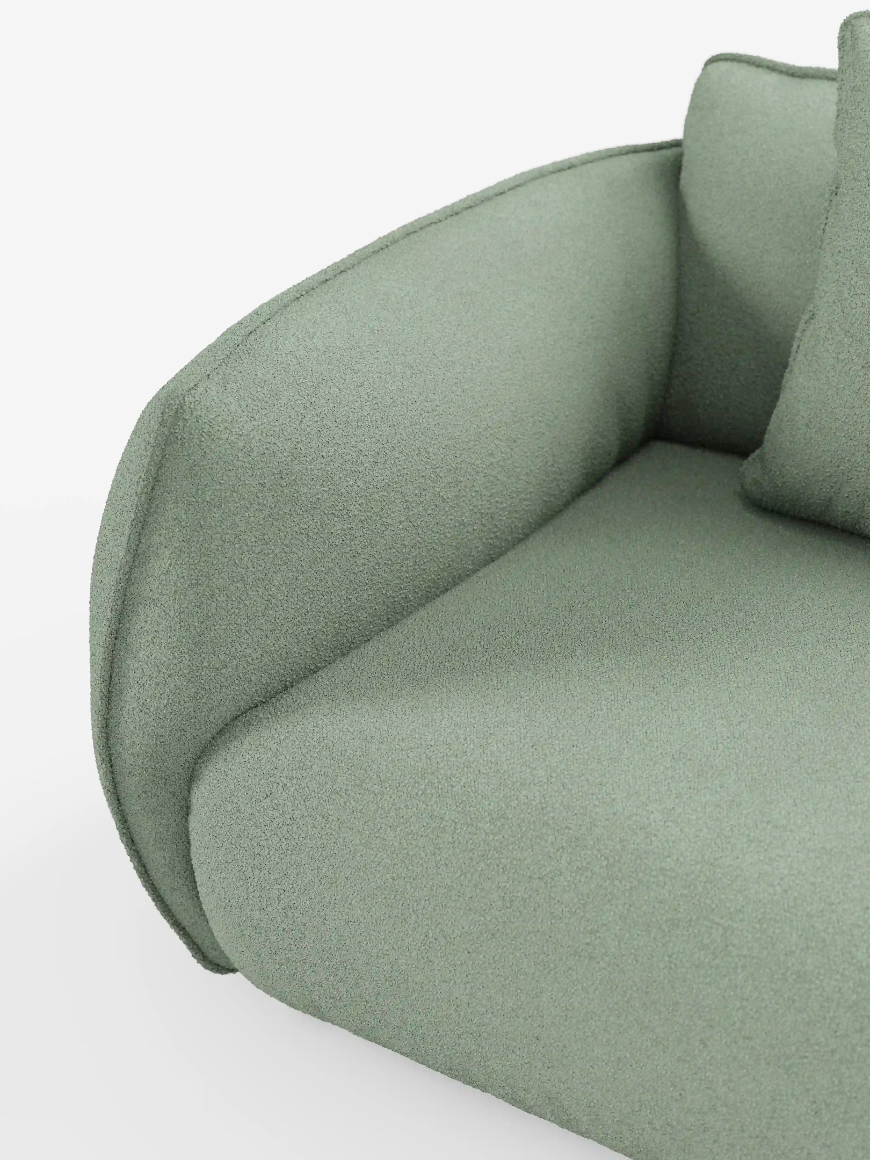 Primo piano del divano angolare con penisola componibile Nimbus di Divani.Store, rivestito in tessuto T33 resistente alle macchie, color verde salvia chiaro, dall’effetto morbido simile al cotone. Questo divano moderno — noto anche come “divano moderno” — presenta braccioli e cuscini di seduta arrotondati, con una superficie dalla trama delicatamente ruvida. Su uno sfondo bianco minimalista, sul lato destro è visibile una parte di un cuscino coordinato.