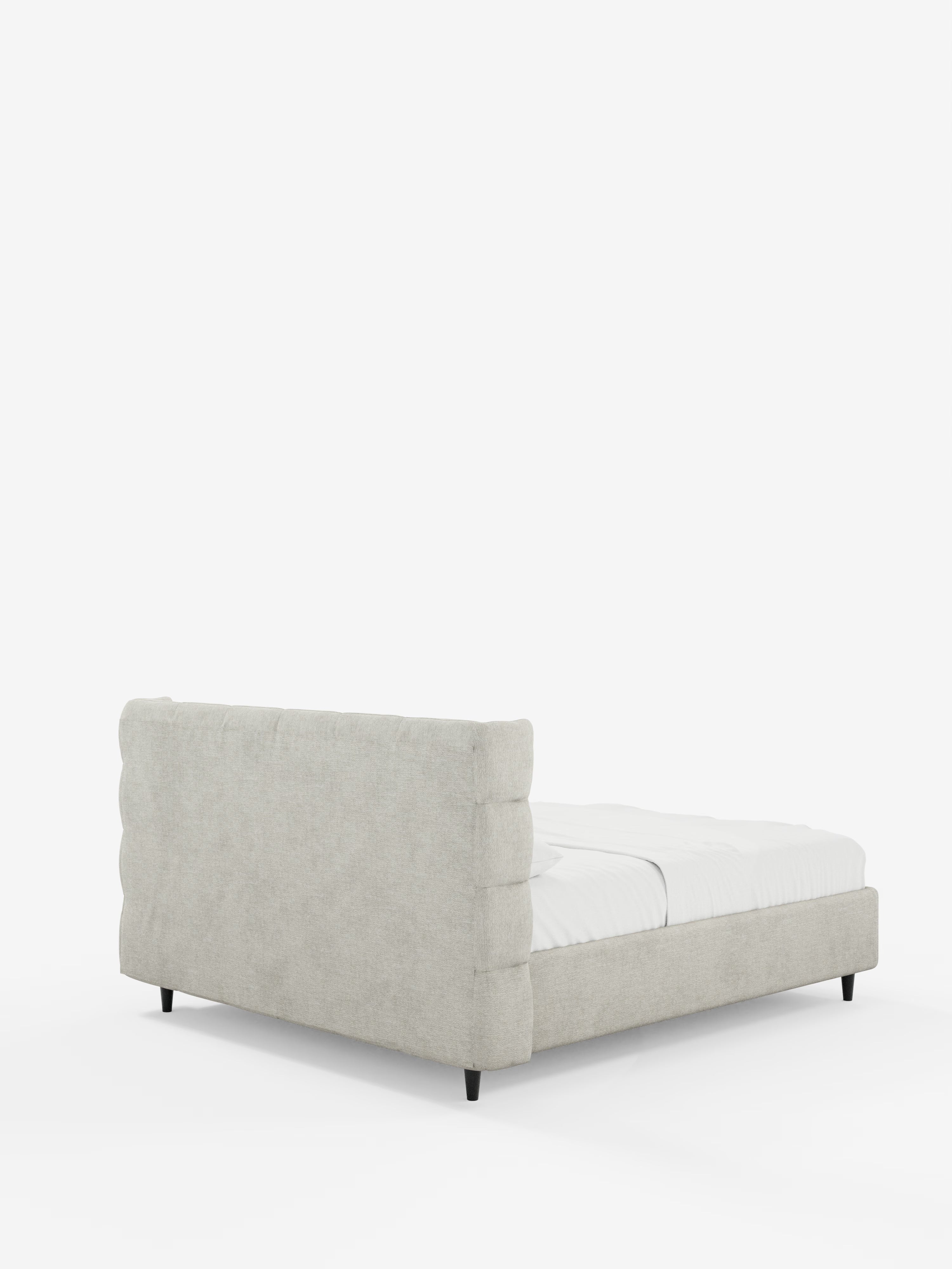 Un letto RAGNAR grigio chiaro imbottito con contenitore e testiera capitonné avvolgente di Letti., caratterizzato da un'elegante finitura imbottita certificata Oeko-Tex®, testiera e pediera imbottite e trapuntate a canali, una silhouette dal profilo basso con gambe corte nere, rivestito con biancheria da letto bianca e posto su uno sfondo bianco a tinta unita.