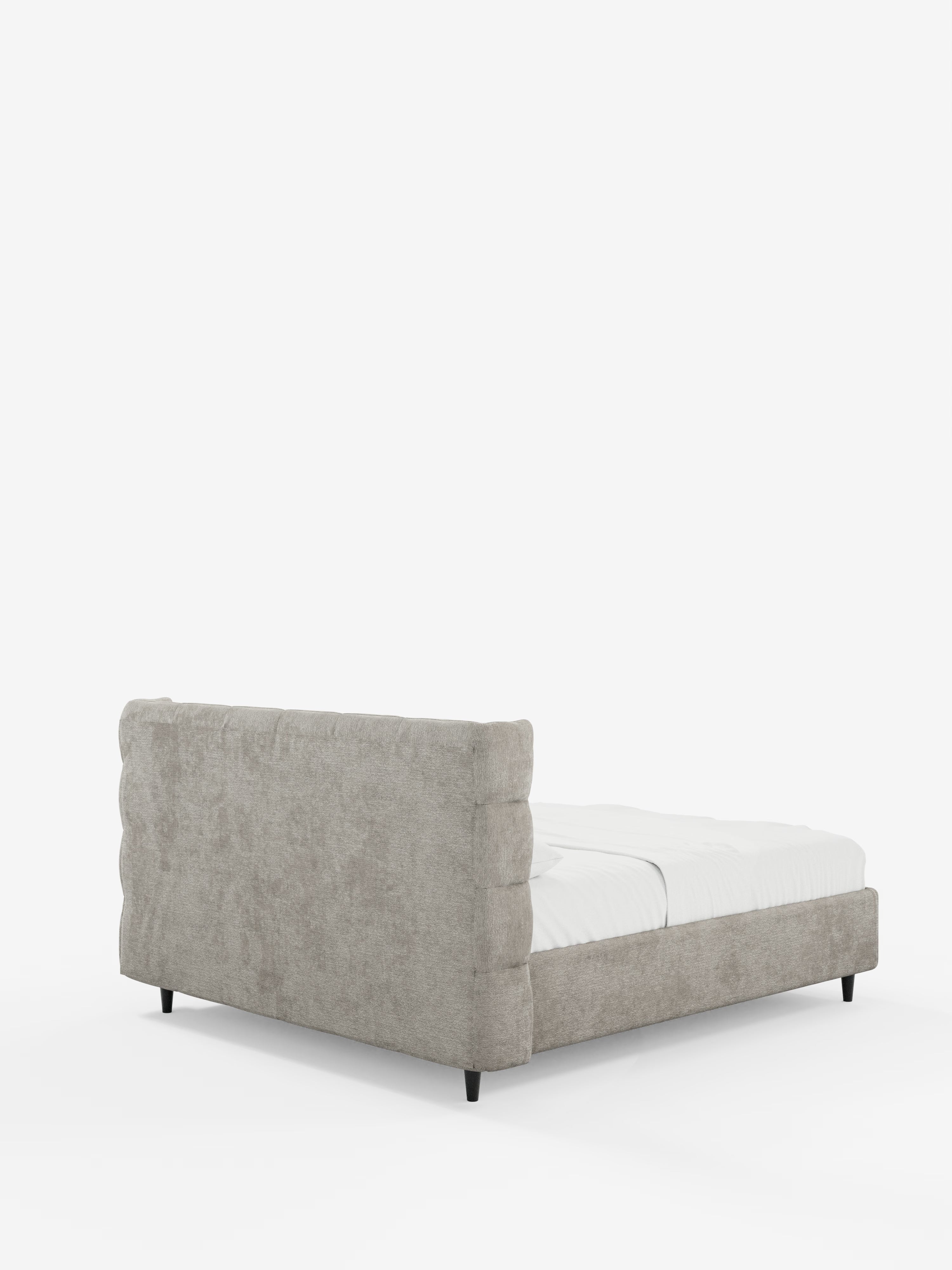 Un letto imbottito contemporaneo RAGNAR con contenitore e testiera capitonné avvolgente di Letti.store, caratterizzato da un elegante tessuto grigio chiaro certificato Oeko-Tex® e da un’alta testiera imbottita avvolgente. Ritratto dall'angolo posteriore sinistro, il letto poggia su corte gambe nere ed è abbinato a biancheria da letto bianca su uno sfondo bianco a tinta unita.