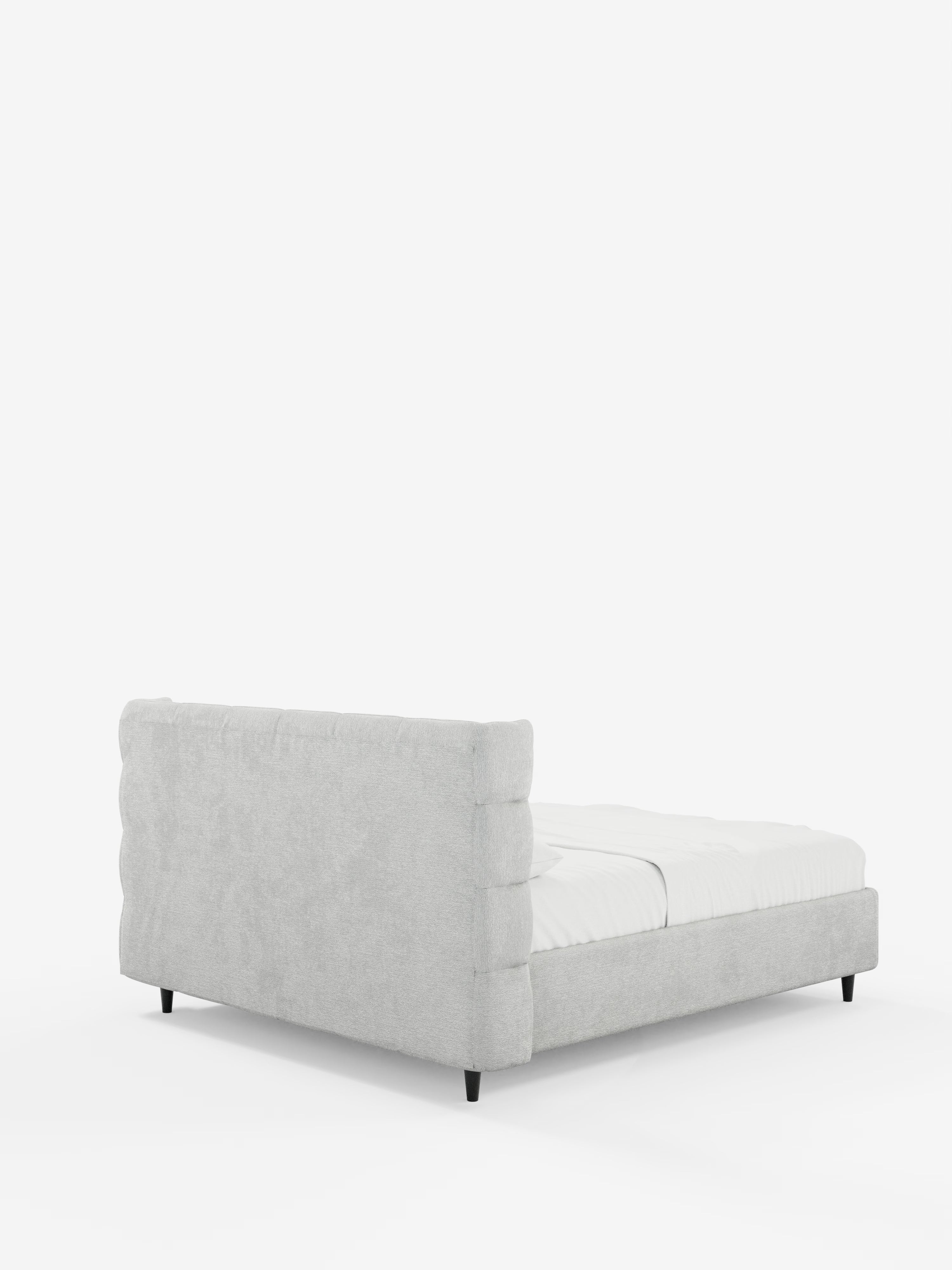 Un letto imbottito RAGNAR dal profilo basso e dallo stile contemporaneo, con contenitore e testiera capitonné avvolgente, firmato Letti.store, caratterizzato da un’elegante struttura imbottita in grigio chiaro certificata Oeko-Tex® con testiera e pediera rettangolari capitonné, completata da raffinate gambe affusolate nere. Il letto è abbinato a una semplice biancheria da letto bianca e fa da contrappunto a uno sfondo bianco a tinta unita.