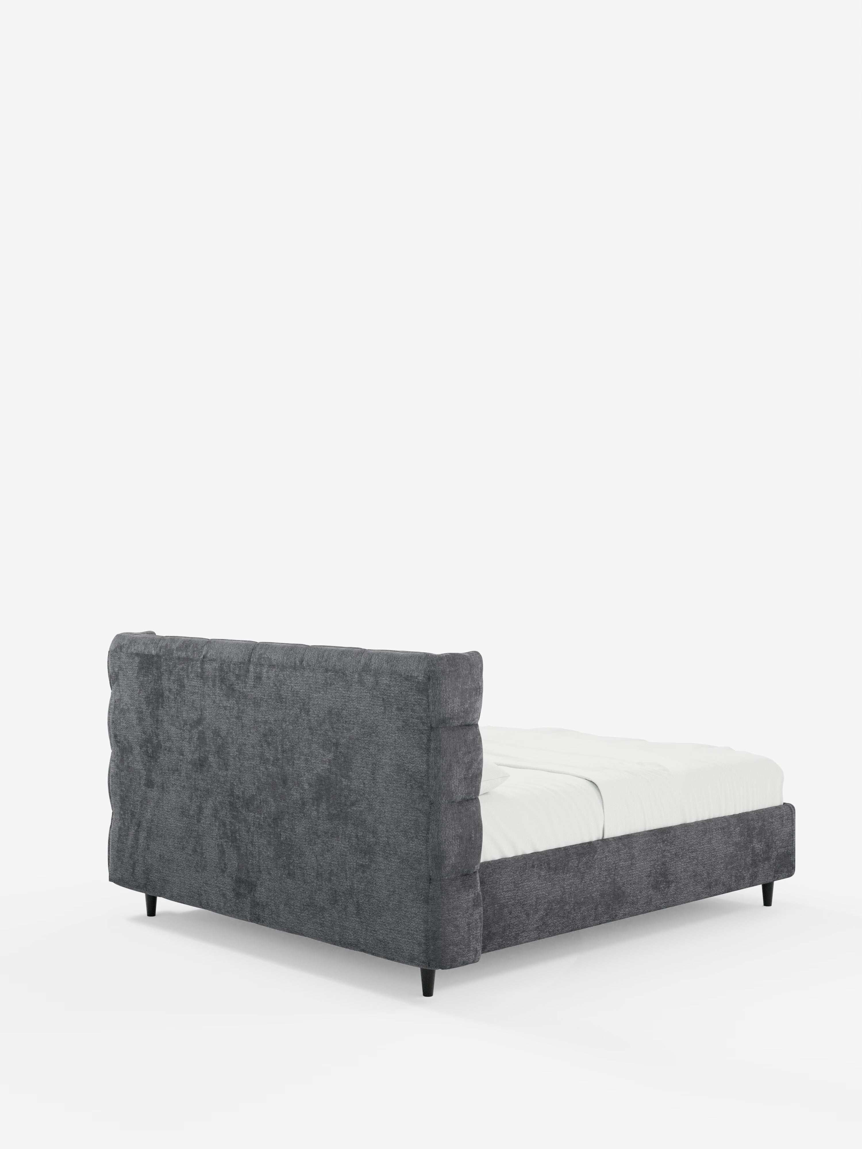 Il letto imbottito RAGNAR con contenitore e testiera capitonné avvolgente di Letti.store è un letto imbottito moderno caratterizzato da un’elegante struttura in tessuto grigio scuro testurizzato, certificato Oeko-Tex®, e da una suggestiva testiera capitonné avvolgente. Presentato in posizione obliqua, il profilo ribassato del letto, con le sue corte gambe nere, è valorizzato da un materasso e da una biancheria da letto bianchi, il tutto su uno sfondo bianco a tinta unita.