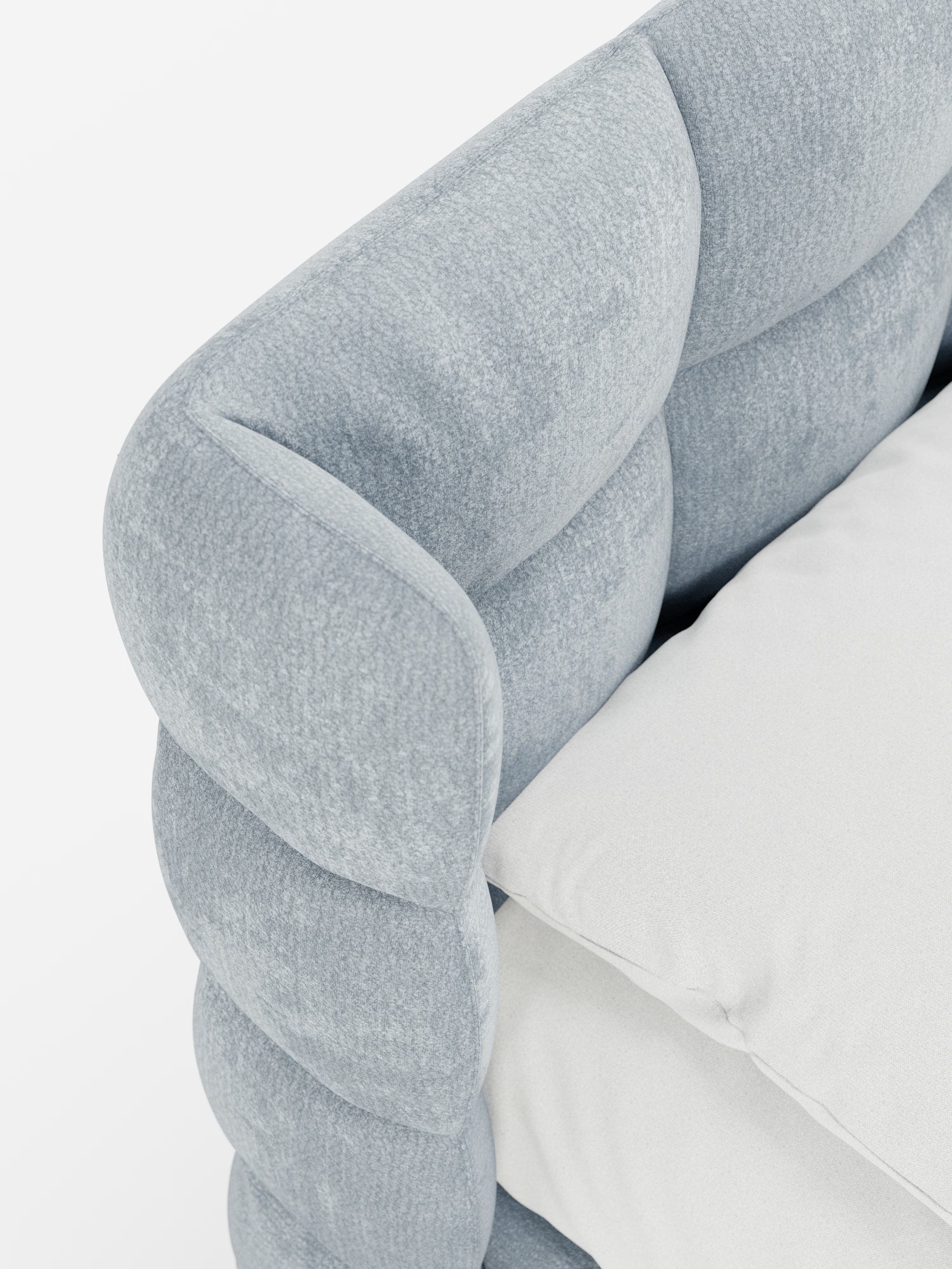 Primo piano del letto imbottito RAGNAR di Letti.store, caratterizzato da una testiera avvolgente capitonné rivestita in un elegante tessuto azzurro certificato Oeko-Tex® dalla morbida trama trapuntata. Un cuscino bianco candido poggia contro la morbida testiera azzurra, creando un contrasto di grande effetto. Lo sfondo minimalista è leggero e ordinato, mettendo in risalto il design sofisticato del letto.