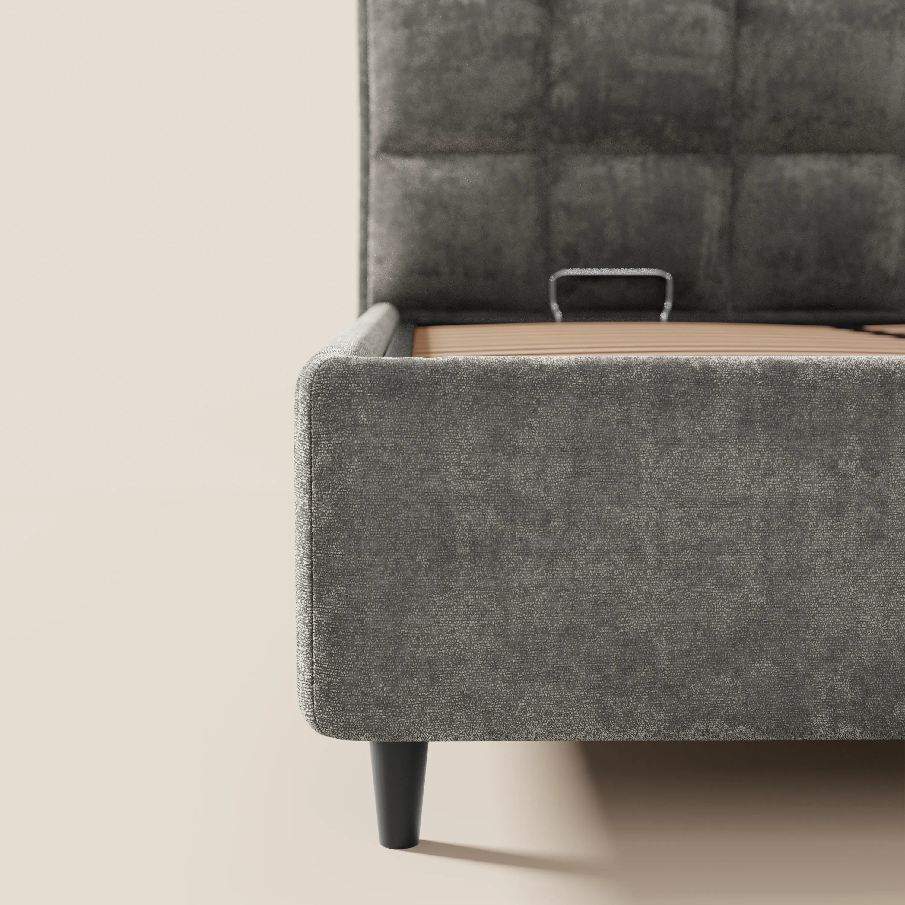 Primo piano del letto imbottito AURO di Letti.store in ciniglia grigio scuro certificata Oeko-Tex®, con testiera alta capitonné, sponde basse, gambe nere e vano contenitore a vista. Il letto è sfatto su uno sfondo neutro.