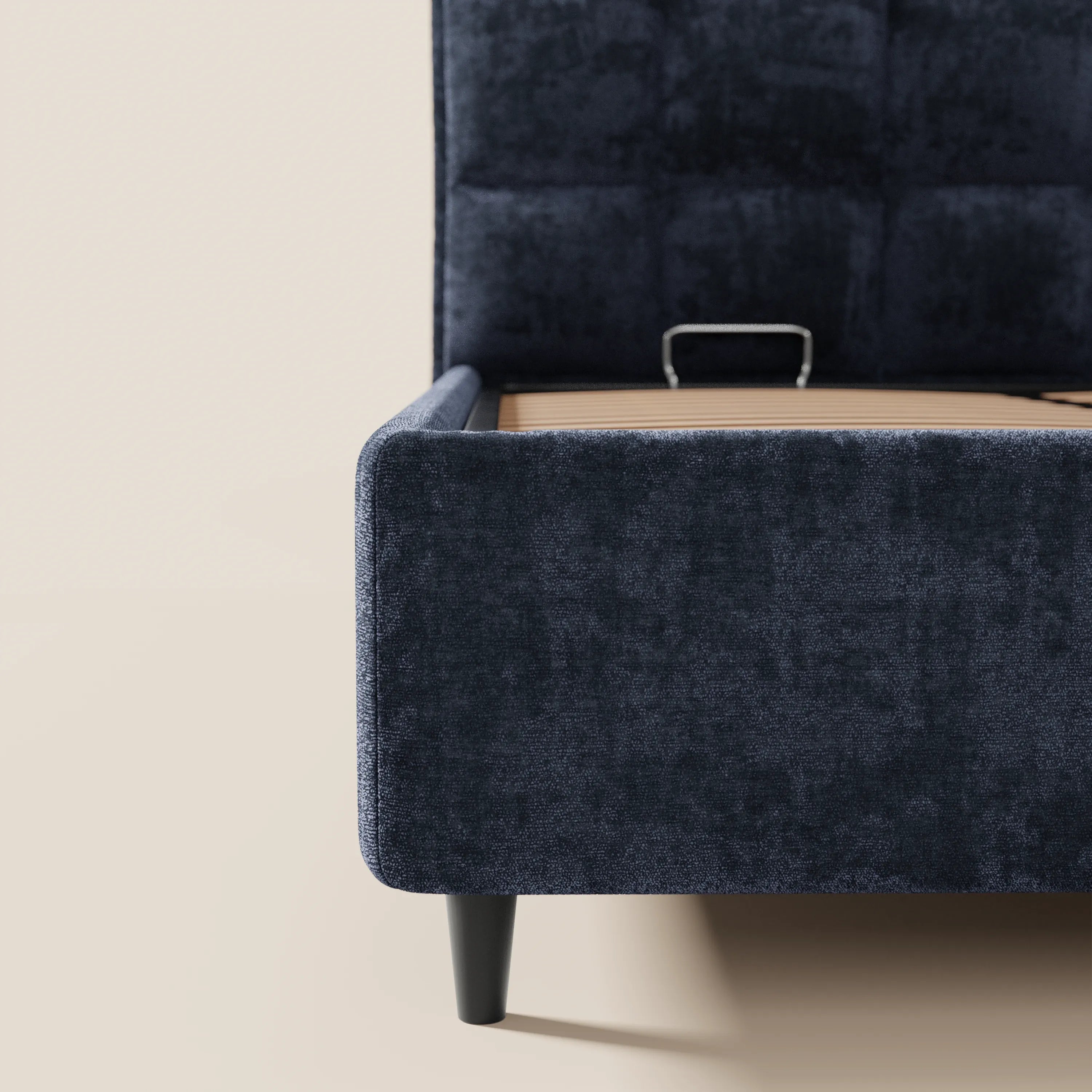 Un primo piano del letto imbottito AURO con contenitore e testiera alta capitonné in ciniglia Oeko-Tex® di Letti.store, con morbido rivestimento blu scuro, gambe nere e una testiera alta a motivi quadrati su sfondo beige chiaro.