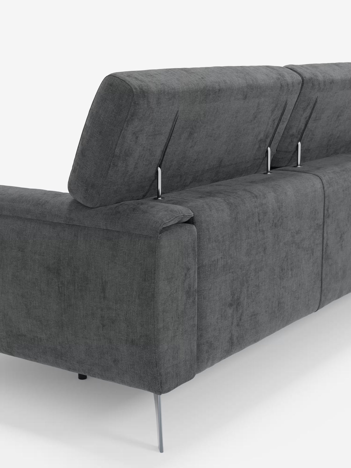 Il divano Caravaggio a 4 posti con tre sedute scorrevoli di Divani.Store è ripreso dal retro su uno sfondo bianco. Questo moderno divano grigio scuro è dotato di poggiatesta regolabili sostenuti da staffe argentate e di sottili gambe in metallo, e si caratterizza per le linee pulite e minimaliste, con un rivestimento in tessuto T31 testurizzato e facile da pulire.