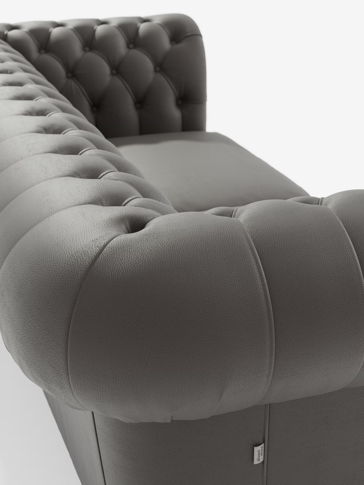 Primo piano del bracciolo e dello schienale di Chester, un divano in pelle grigia trapuntata caratterizzato da profondi bottoni decorativi. Questo Chesterfield di Divani.Store offre un'imbottitura morbida ed elegante e un'eleganza senza tempo come divano Chesterfield in vera pelle spessorata a 2 e 3 posti, realizzato artigianalmente in Italia e presentato su uno sfondo bianco a tinta unita.