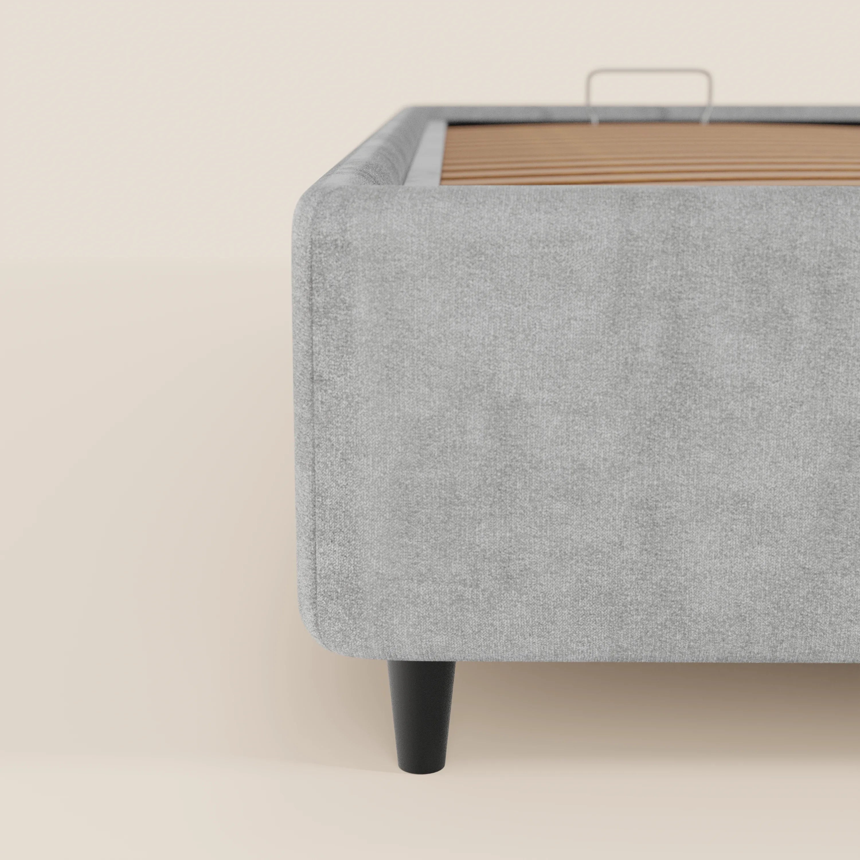 Una vista laterale ravvicinata del letto sommier ERON di Letti.store, realizzato in tessuto impermeabile grigio chiaro certificato Oeko-Tex, con gambe angolari in legno nero e una base contenitiva con doghe in legno a vista, il tutto su uno sfondo beige chiaro.