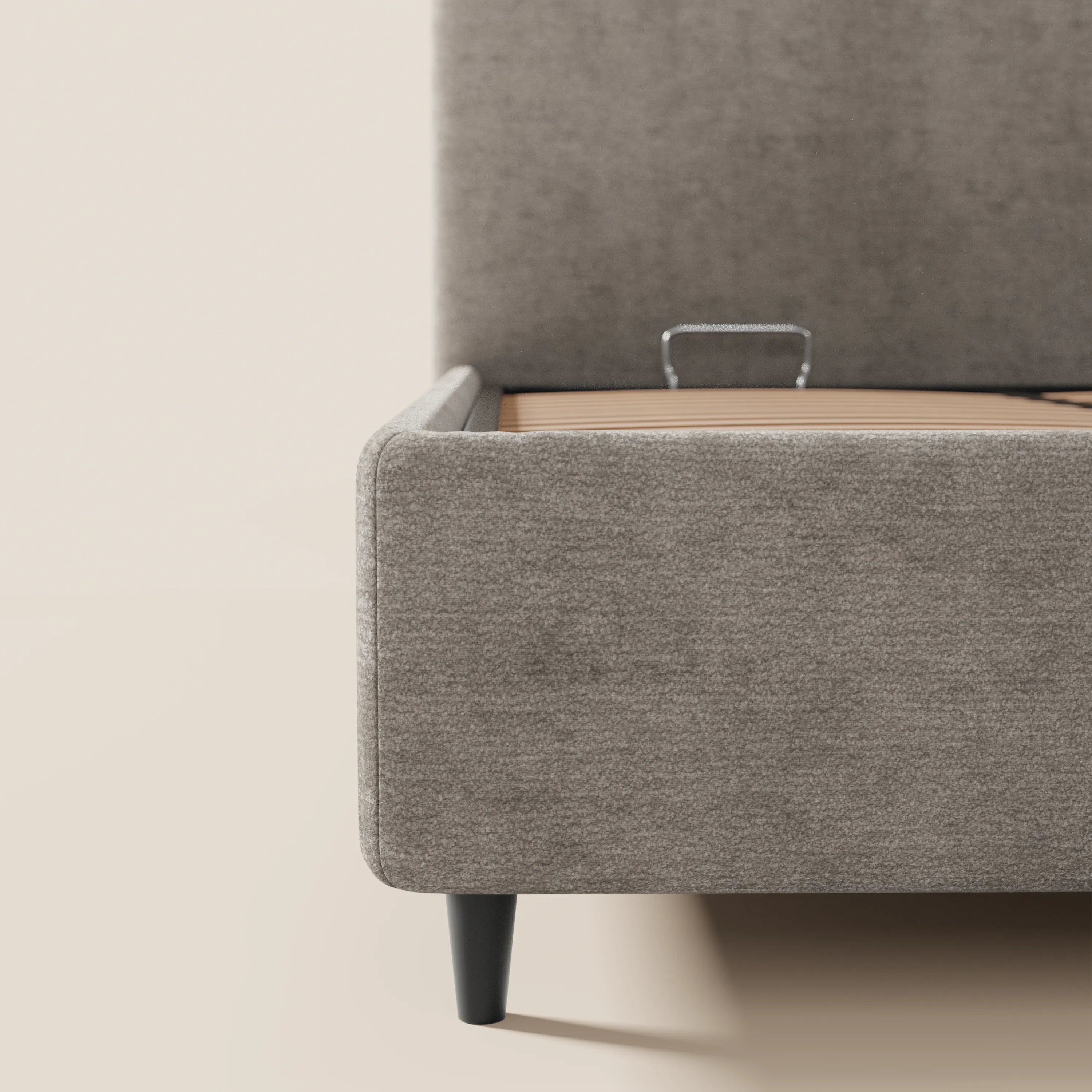 Primo piano del letto imbottito KAELOS minimal di Letti.store, in ciniglia grigio chiaro con gambe alte nere, testiera arrotondata e vano contenitore. Il design minimalista è messo in risalto dalla struttura metallica a vista che sostiene il materasso, che spicca su uno sfondo neutro.
