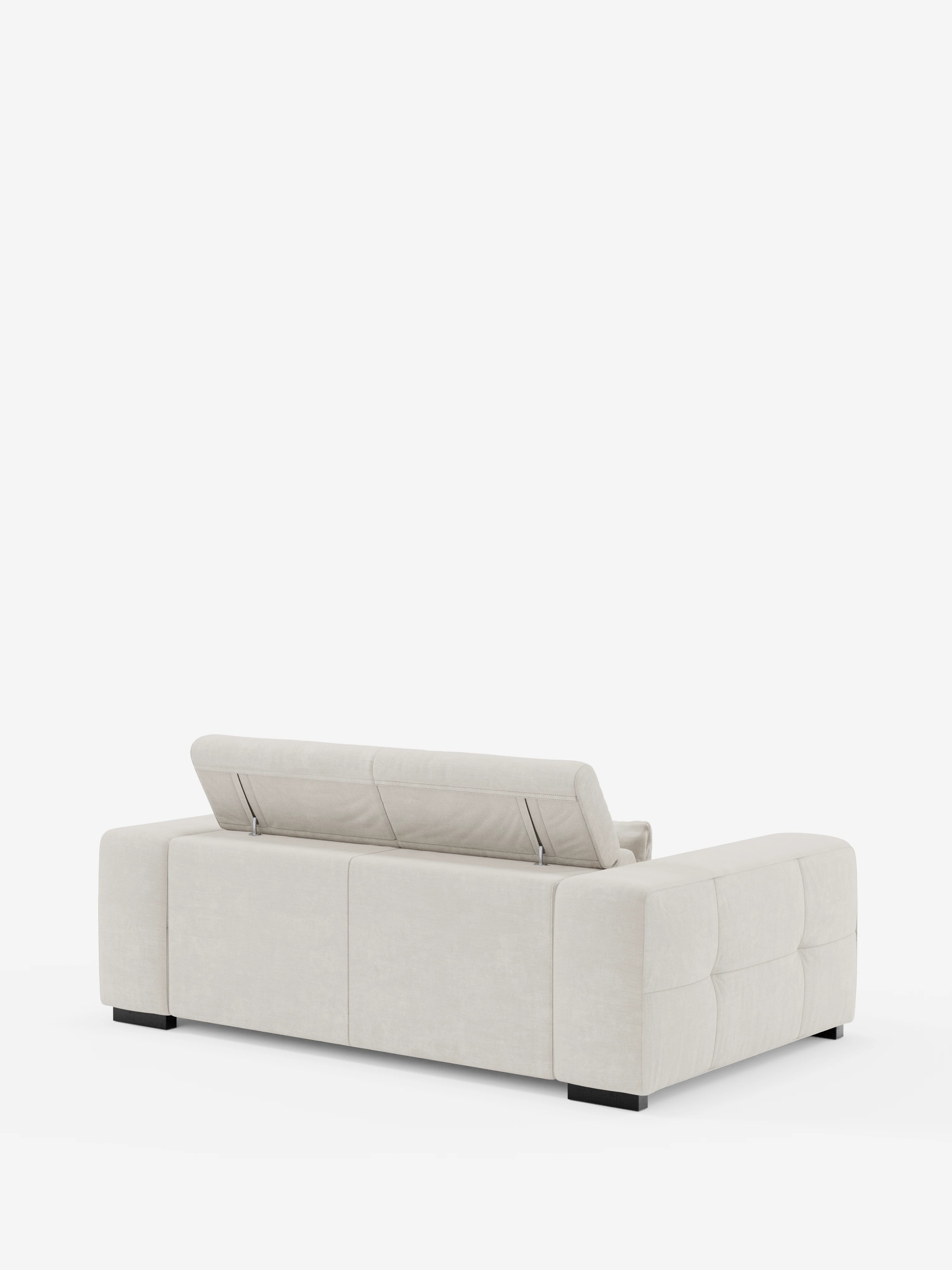 Un moderno divano Monarch color beige chiaro di Divani.Store visto da dietro; questo «Divano con relax elettrico per l’allungamento delle sedute e poggiatesta reclinabile in tessuto morbido smacchiabile T31» presenta un profilo basso, ampi braccioli imbottiti, piedini a blocco neri, fianchi trapuntati e un poggiatesta regolabile parzialmente sollevato sul lato sinistro dello schienale.