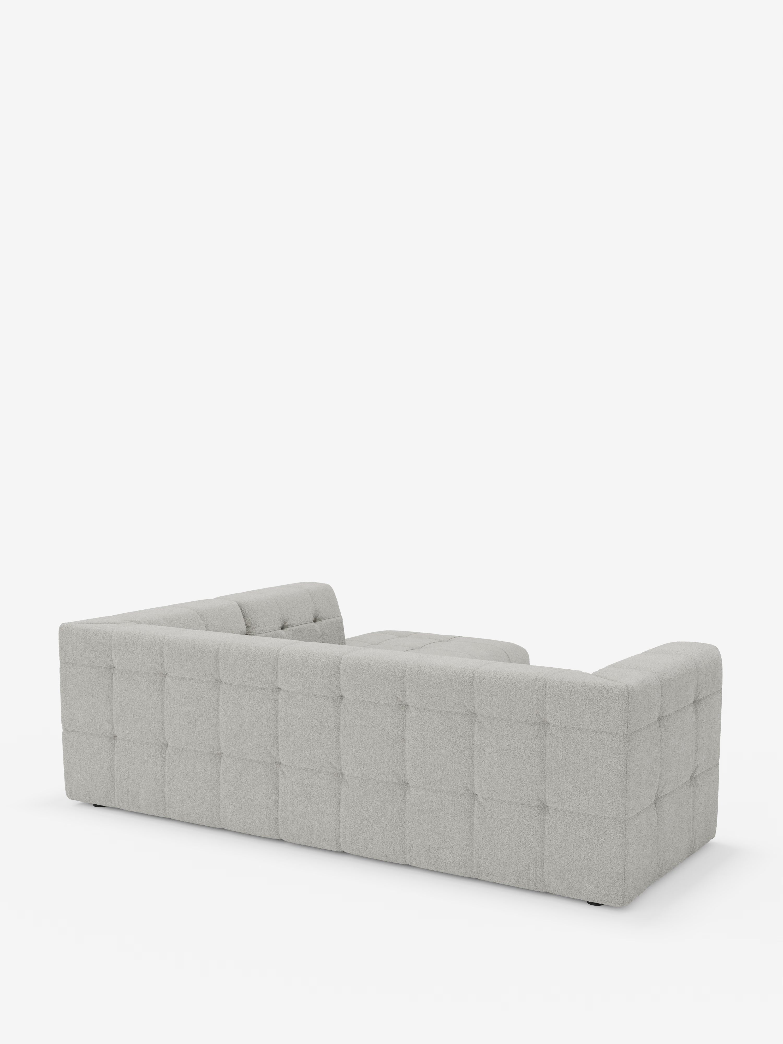 Un divano angolare componibile e modulare Mosaic, dal colore grigio chiaro, moderno e dal profilo basso, realizzato in bouclé: capitonné e design in tessuto smacchiabile T21 di Divani.Store, è raffigurato di retro su uno sfondo bianco a tinta unita. I braccioli e lo schienale sono della stessa altezza e presentano un motivo trapuntato a griglia, rendendolo l’aggiunta perfetta a qualsiasi soggiorno moderno.