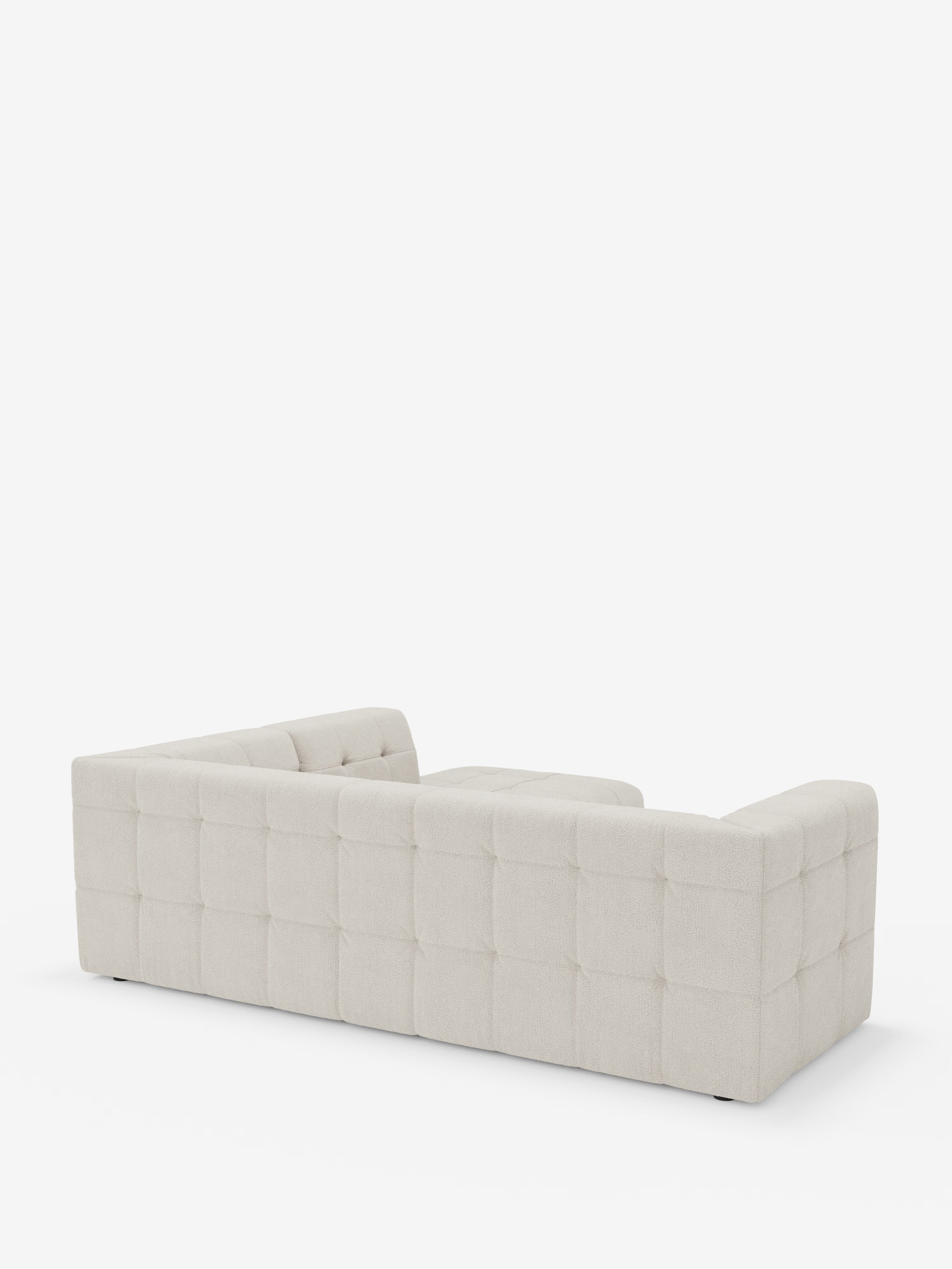 Un ampio e moderno divano angolare componibile e modulare Mosaic in bouclé: capitonné e design in tessuto smacchiabile T21 di Divani.Il modello Store, in bianco sporco con dettagli quadrati trapuntati lungo i lati e lo schienale e un raffinato rivestimento in bouclé, è ripreso da dietro e leggermente a sinistra, su uno sfondo bianco a tinta unita.