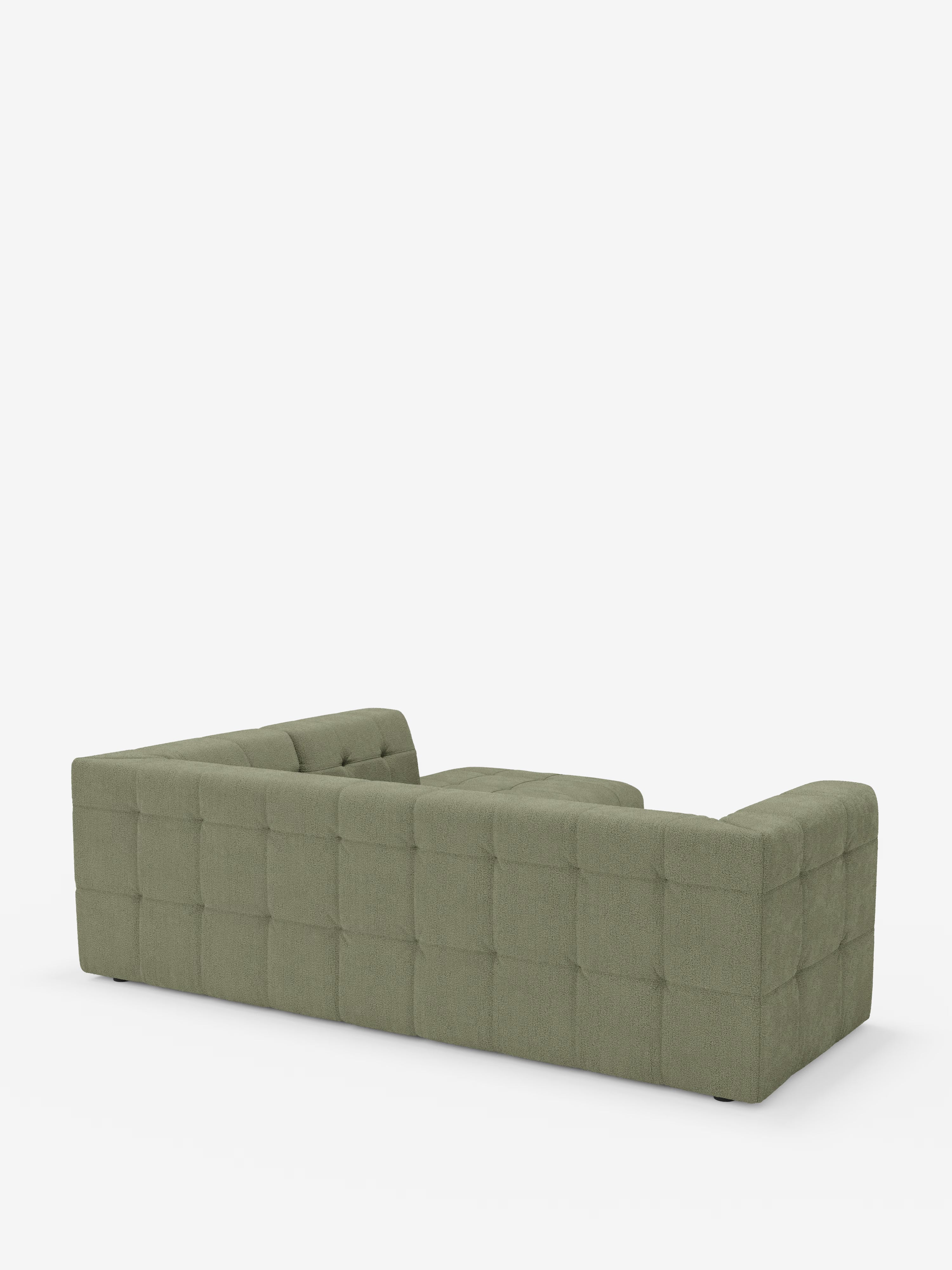 Un divano angolare componibile e modulare Mosaic di colore verde, realizzato in bouclé da Divani.Store, caratterizzato da una profonda trapuntatura capitonné su tutti i lati visibili, braccioli bassi e schienale ribassato, è ripreso di spalle in posizione angolare su uno sfondo bianco a tinta unita: perfetto per aggiungere stile e comfort a qualsiasi soggiorno moderno. Il tessuto T21 smacchiabile garantisce una facile manutenzione senza compromettere il suo design raffinato.