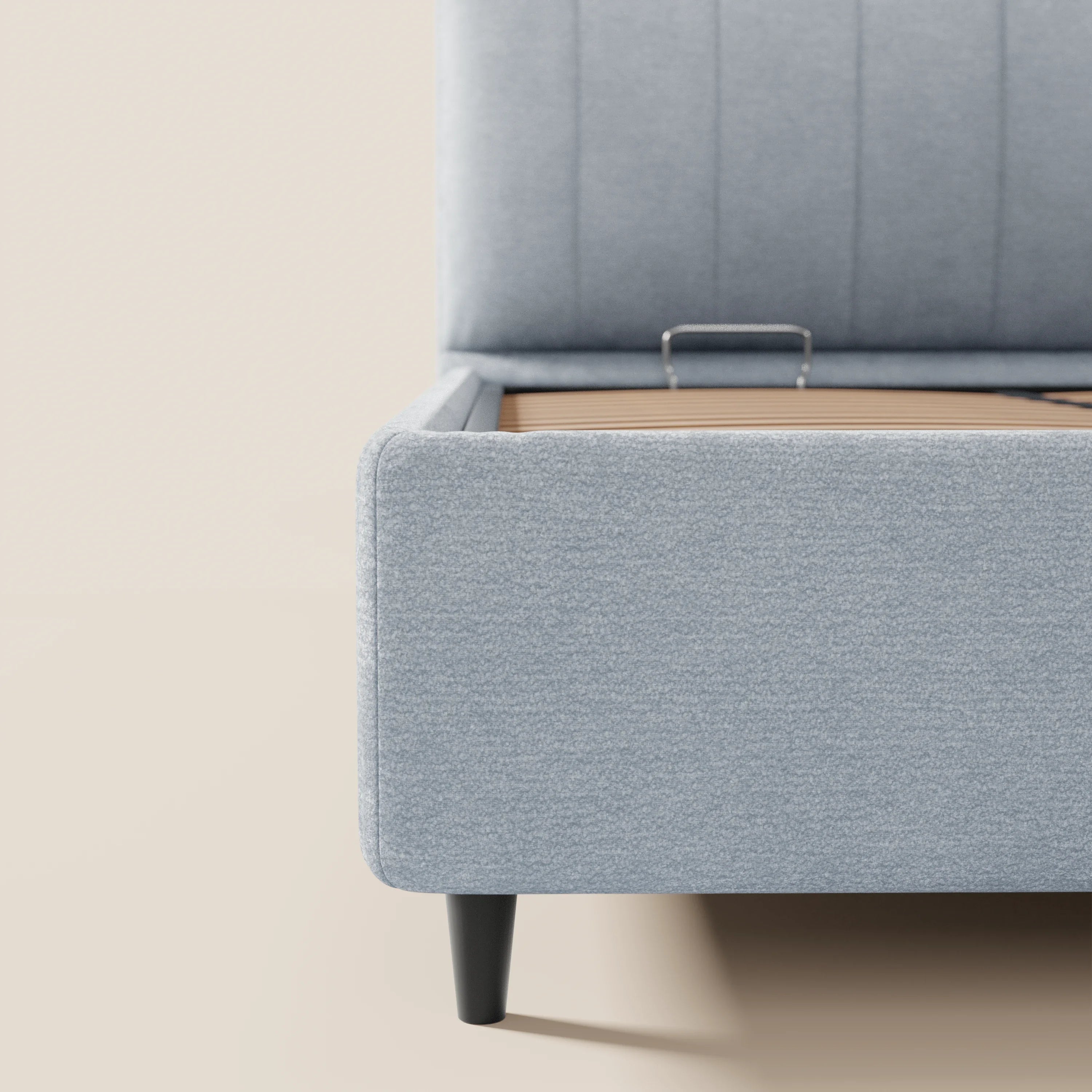 Un primo piano del letto imbottito ONYX con vano contenitore e testiera verticale in tessuto Oeko-Tex® di Letti.store, caratterizzato da gambe nere e spazio di stivaggio sotto il letto, raffigurato su uno sfondo beige.