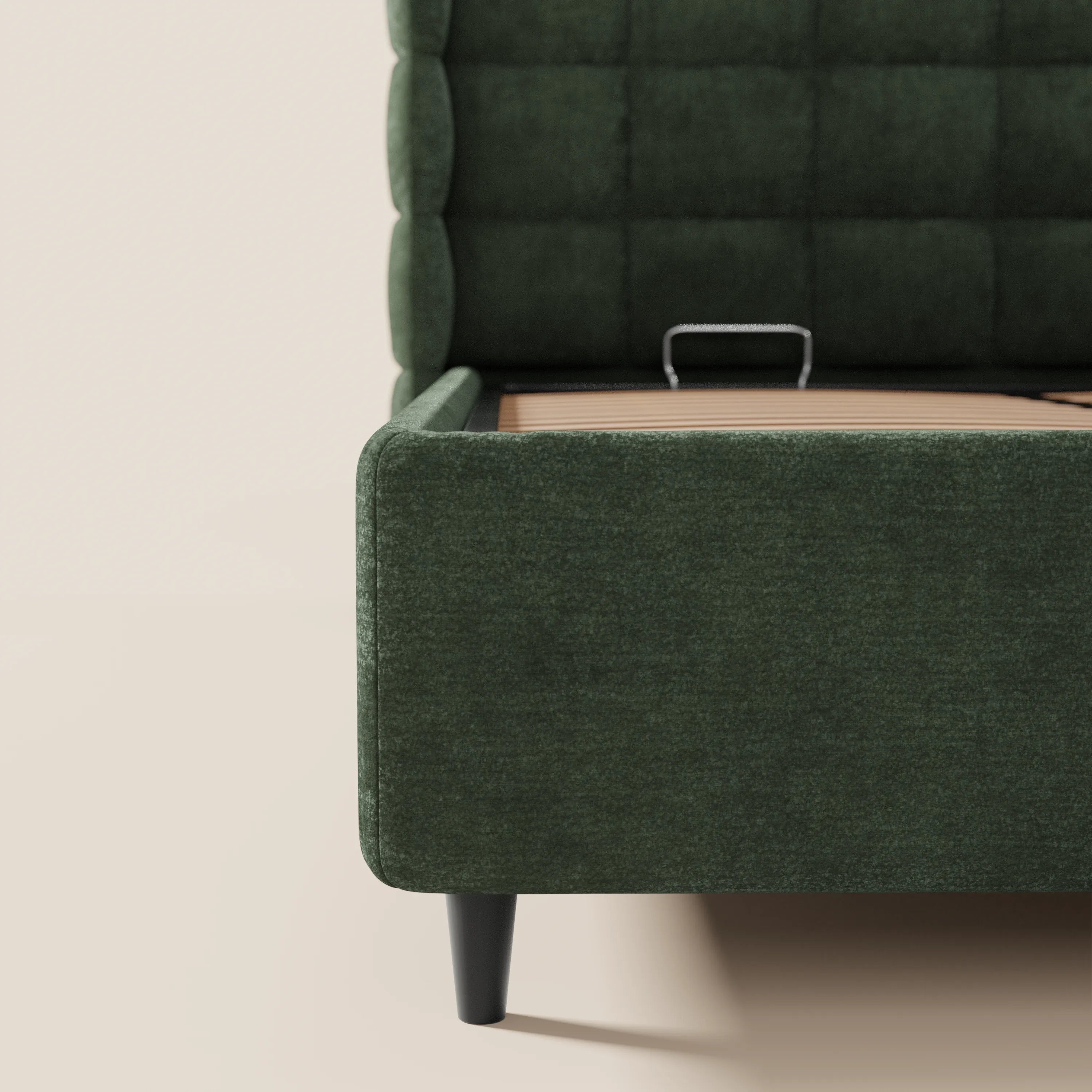 Primo piano del letto imbottito RAGNAR di Letti.store in tessuto verde scuro certificato Oeko-Tex®, caratterizzato da una testiera capitonné con trapuntatura a griglia e da un vano contenitore sotto il letto con base a doghe in legno e maniglia in metallo. Sfondo e pavimento in beige neutro.