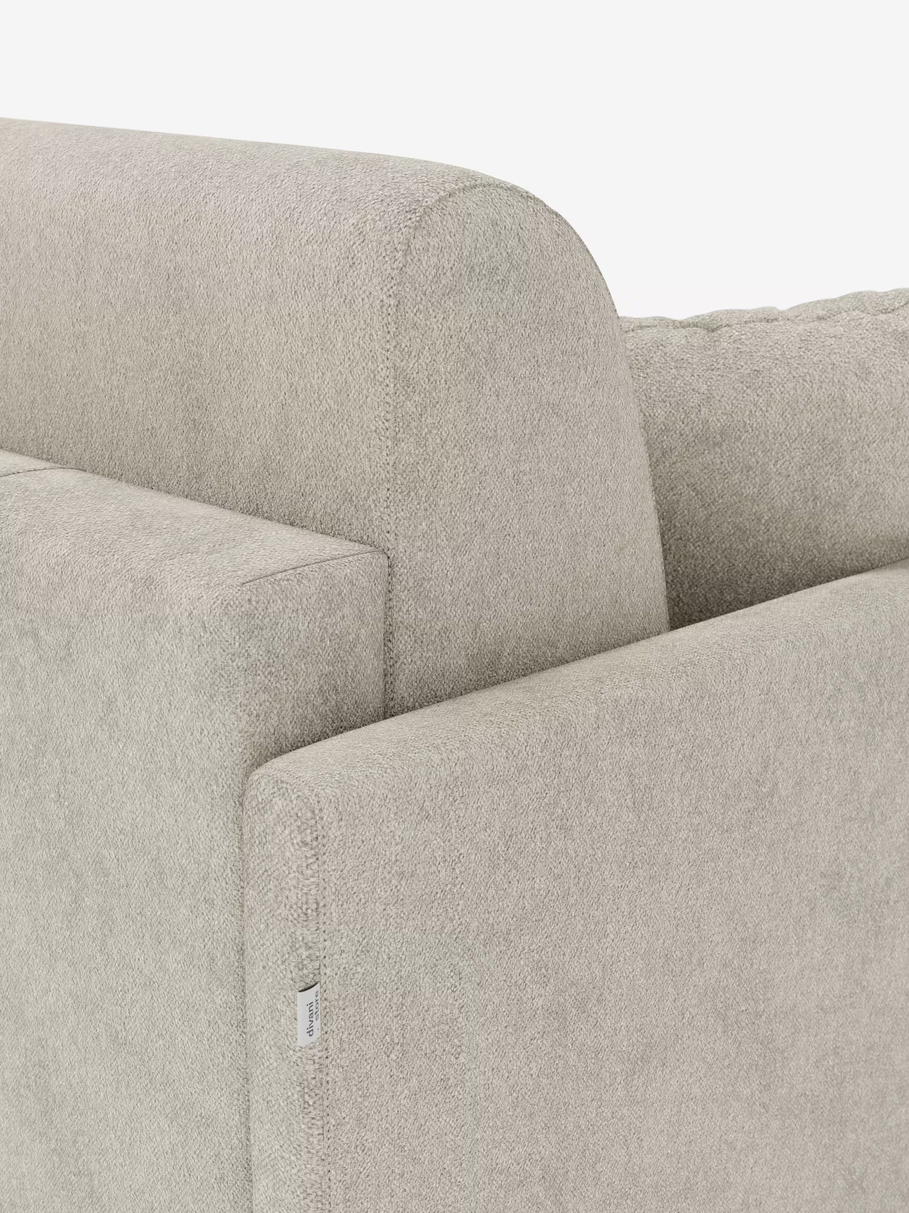 Primo piano dell'angolo di un divano letto Tommy Divano a 2 e 3 posti, color beige chiaro, di Divani.Store, rivestito in tessuto T33 antimacchia, simile al cotone e sfoderabile. L'immagine mostra linee pulite, una superficie testurizzata, un bracciolo squadrato con cucitura a vista e una piccola etichetta in tessuto bianco sul bracciolo. Lo sfondo è bianco a tinta unita.