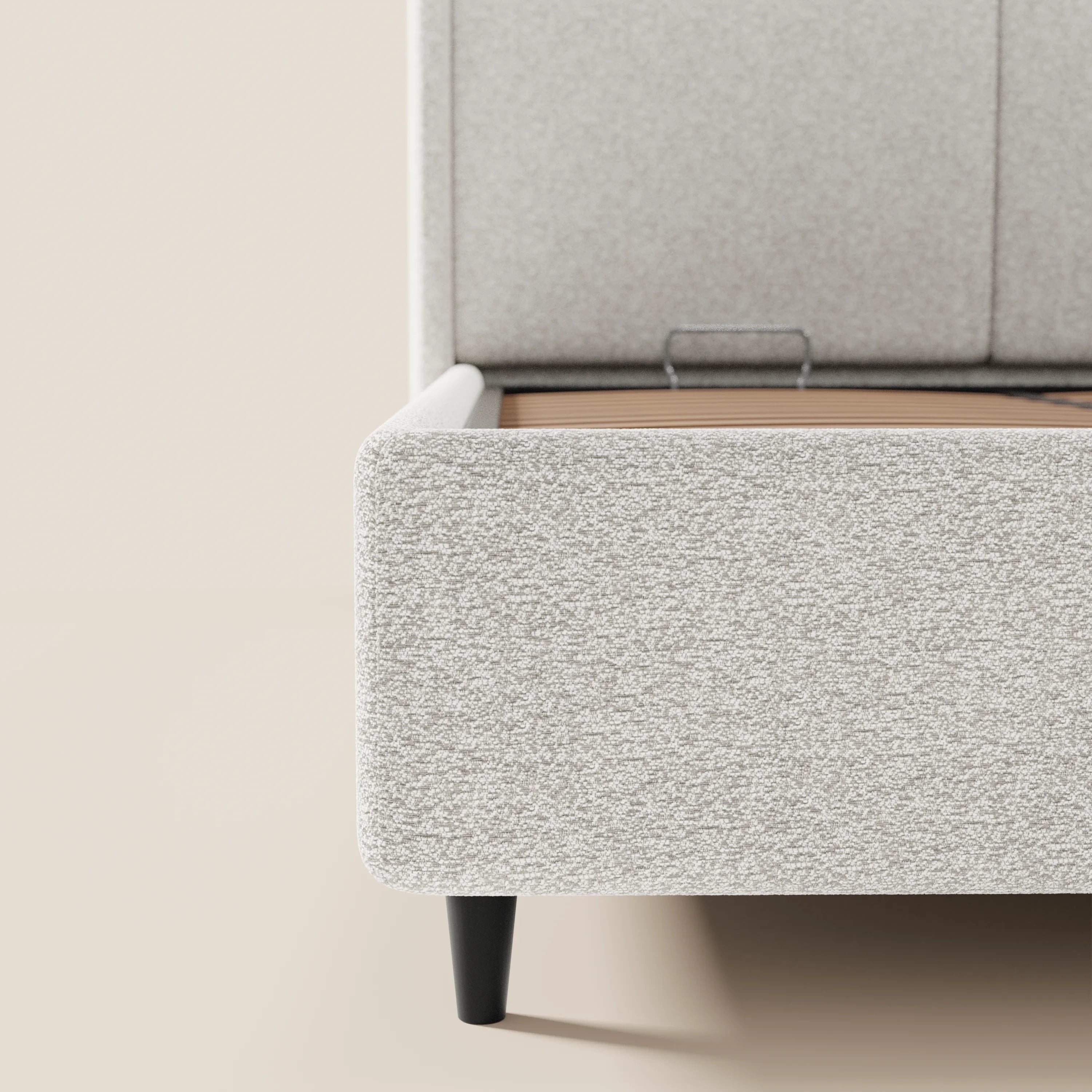 Un primo piano del letto di design VALKIRIA di Letti.store, realizzato in tessuto grigio chiaro certificato Oeko-Tex®, mostra l'angolo sinistro con le gambe corte nere, le linee pulite e la morbida trama, mettendo in risalto il suo look contemporaneo e la testiera avvolgente su uno sfondo neutro.