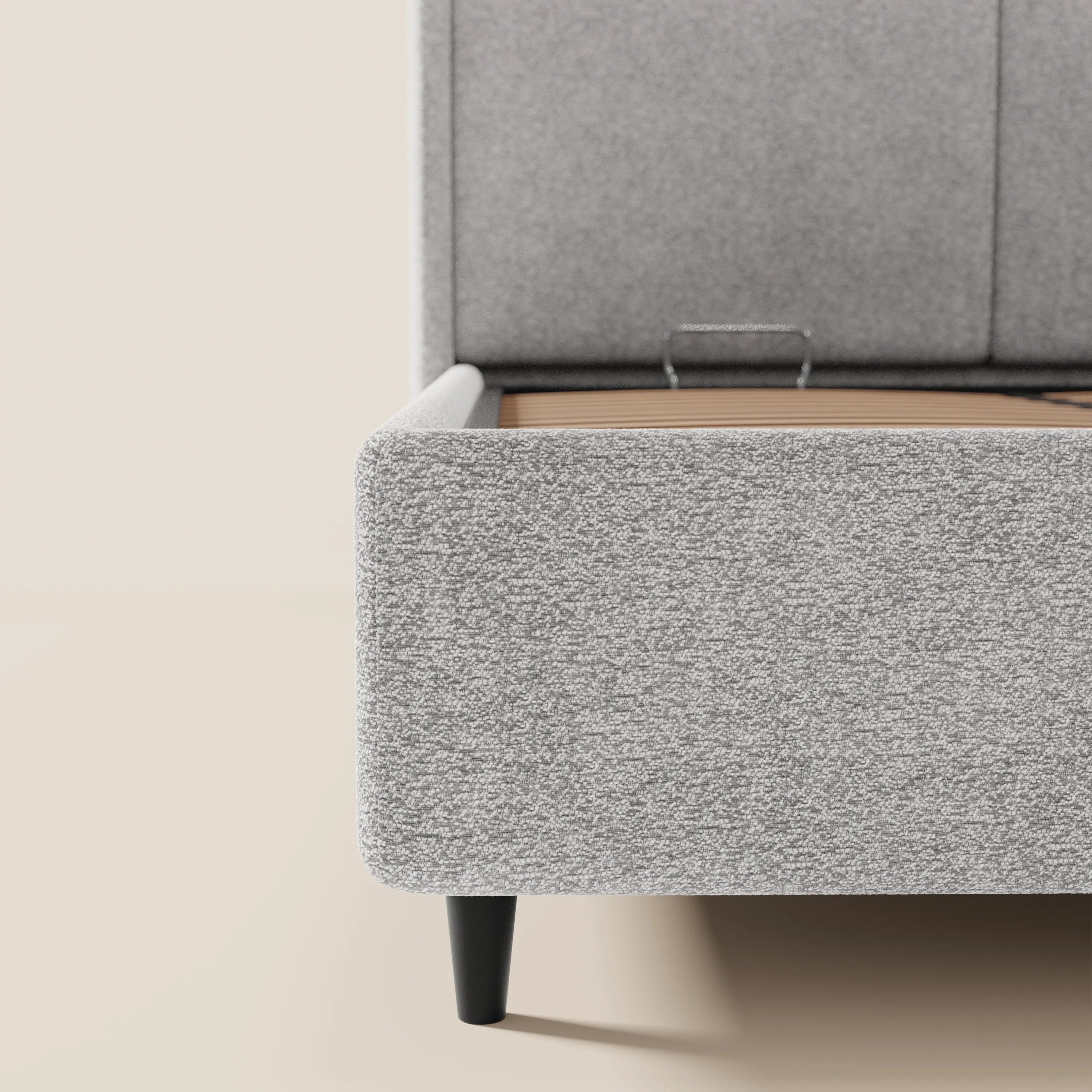 Primo piano del letto di design VALKIRIA di Letti.store, rivestito in tessuto grigio chiaro certificato Oeko-Tex®. Viene mostrato solo il lato sinistro, caratterizzato da 2 cuscini imbottiti, una morbida pediera e gambe corte nere su uno sfondo beige.