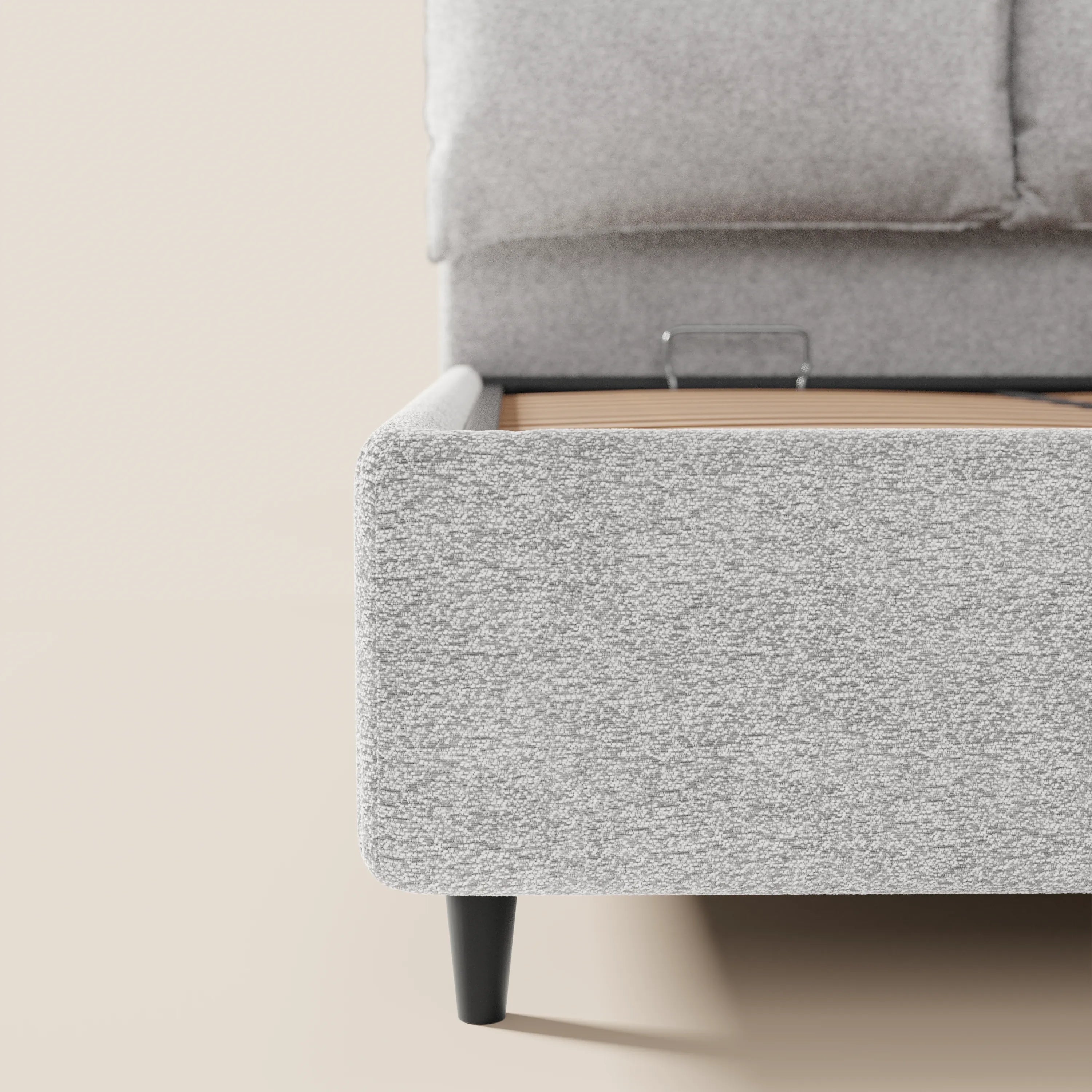 Primo piano del letto imbottito ZAYRON con contenitore di Letti.store, realizzato in tessuto grigio chiaro certificato Oeko-Tex®, che ne mette in risalto la trama del tessuto, le gambe angolate nere, la morbida testiera imbottita e i cuscini regolabili su uno sfondo neutro.