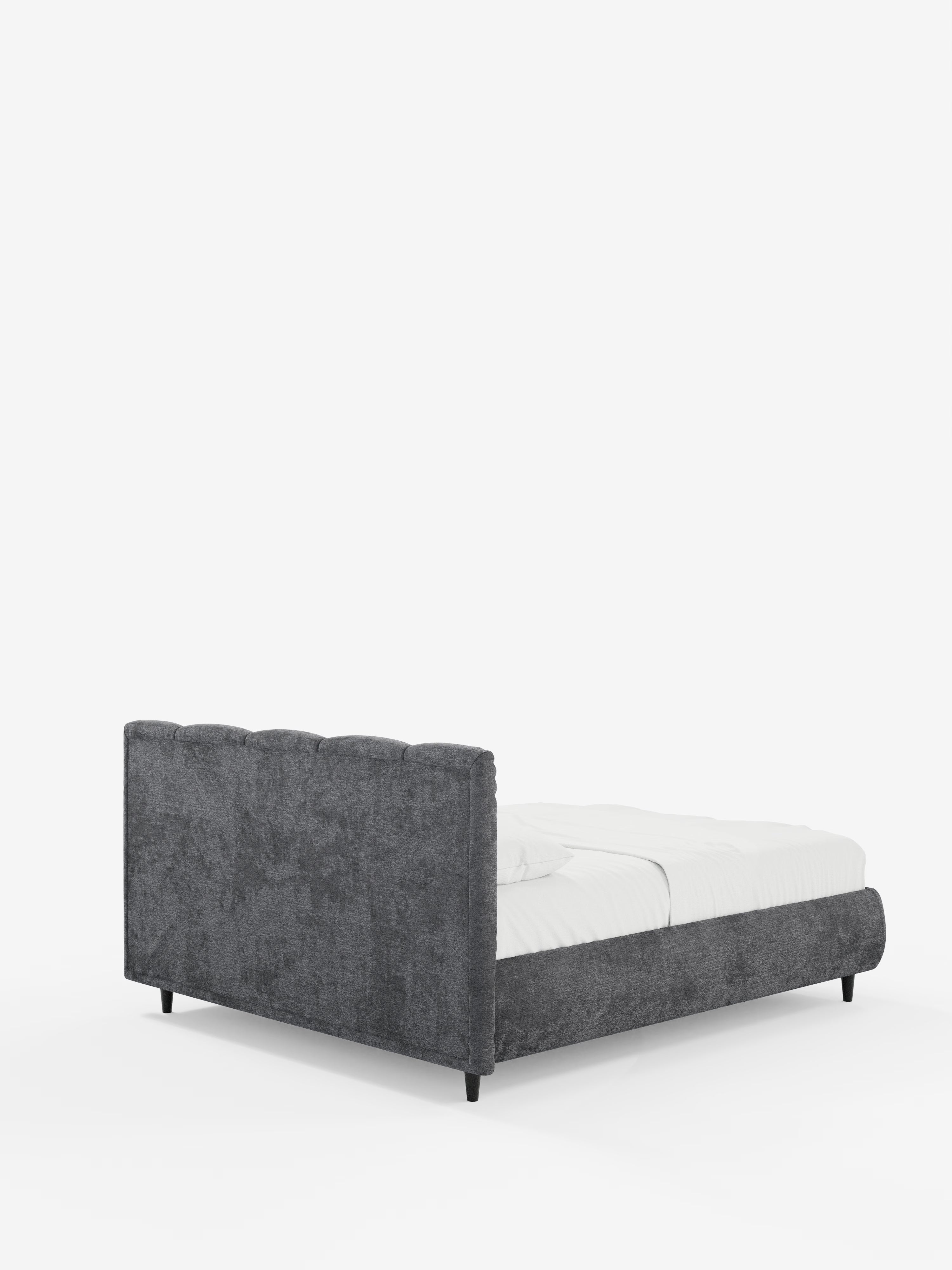 Un letto in stile shabby chic: il modello ARKAM di Letti.store presenta una testiera imbottita con cuciture verticali, realizzata in tessuto certificato Oeko-Tex®. Ripreso da un'angolazione laterale posteriore, questo letto con contenitore è rivestito con biancheria da letto bianca e poggia su gambe nere su uno sfondo bianco a tinta unita.