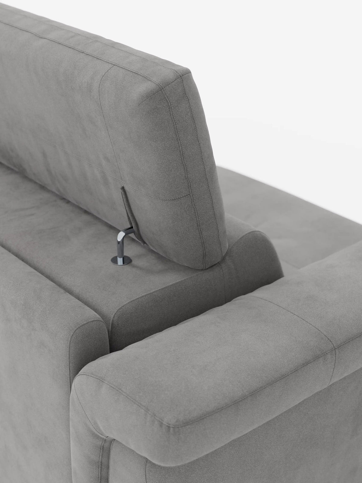 Primo piano del divano letto di design Capri di Divani.Store, caratterizzato da un moderno angolo grigio con poggiatesta reclinabili fissati tramite eleganti aste metalliche. Il raffinato tessuto effetto velluto smacchiabile T30 presenta una morbida consistenza simile alla pelle scamosciata ed è caratterizzato da cuciture lisce e pulite che incarnano la manifattura italiana. Lo sfondo bianco a tinta unita mette in risalto gli eleganti dettagli di design del divano e i suoi caratteristici piedini alti.