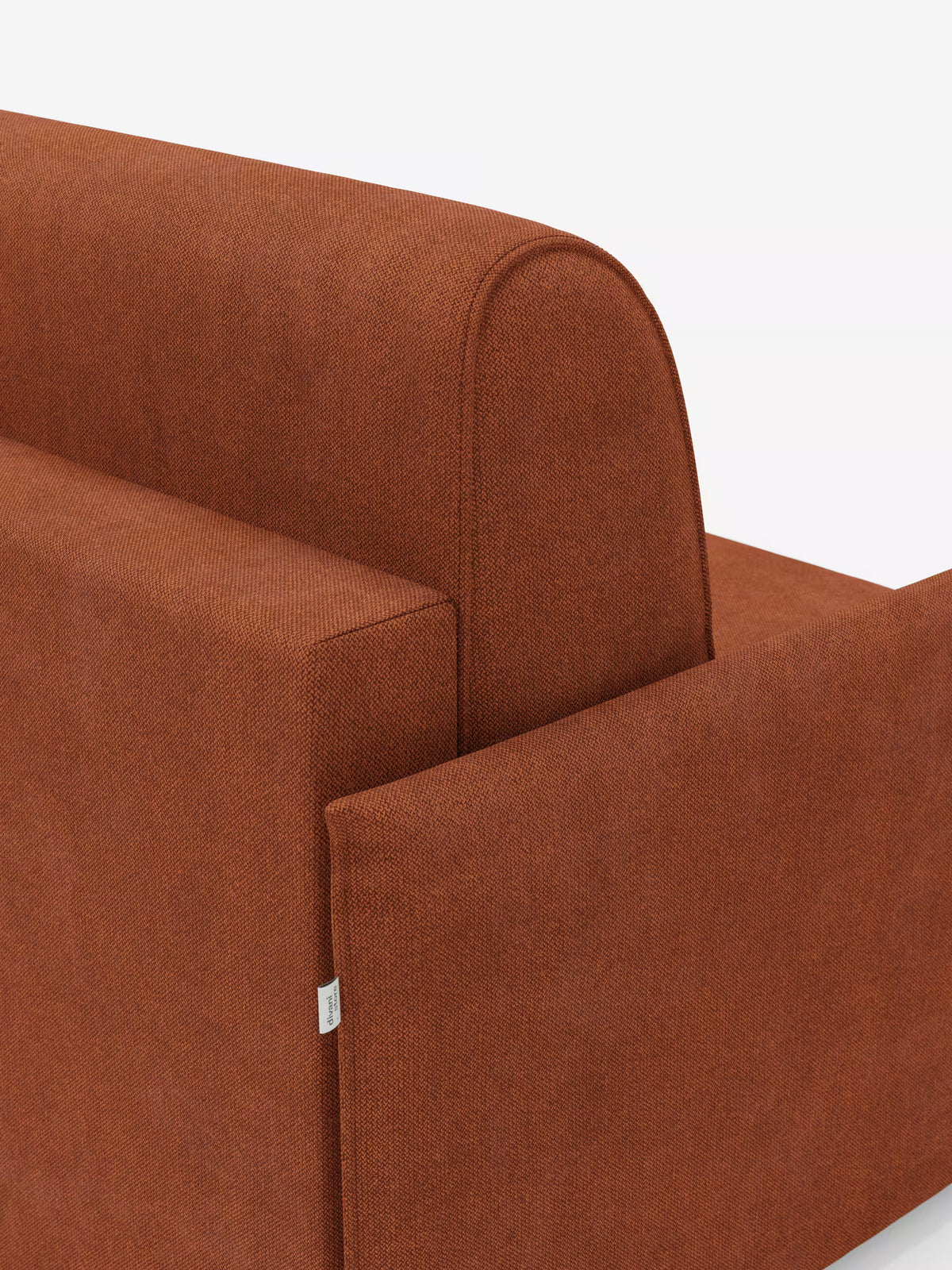 Primo piano della poltrona letto compatta Evans con materasso di Divani.Store, rivestita in tessuto T23 color ruggine e resistente alle macchie, dalle linee pulite e moderne. L’attenzione è concentrata sullo schienale e sui braccioli leggermente arrotondati, che mettono in risalto una piccola etichetta in tessuto con il marchio sul lato. Questa poltrona letto compatta e salvaspazio è ideale per valorizzare qualsiasi ambiente contemporaneo. Ripresa su uno sfondo bianco a tinta unita.