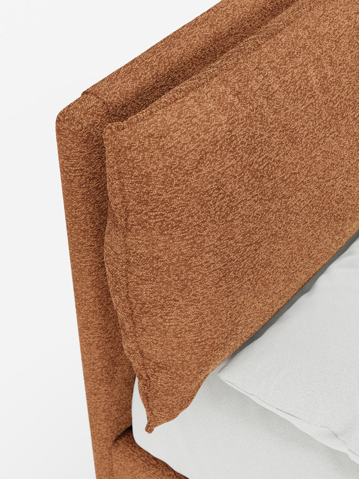 Primo piano di un letto imbottito ZAYRON con contenitore e morbidi cuscini regolabili di Letti.store, che mette in risalto la testiera in tessuto testurizzato color ruggine, certificata Oeko-Tex®, e il morbido cuscino regolabile appoggiato alla testiera regolabile. Sul materasso, su uno sfondo bianco, si intravede una parte di un lenzuolo bianco e di un cuscino grigio chiaro.
