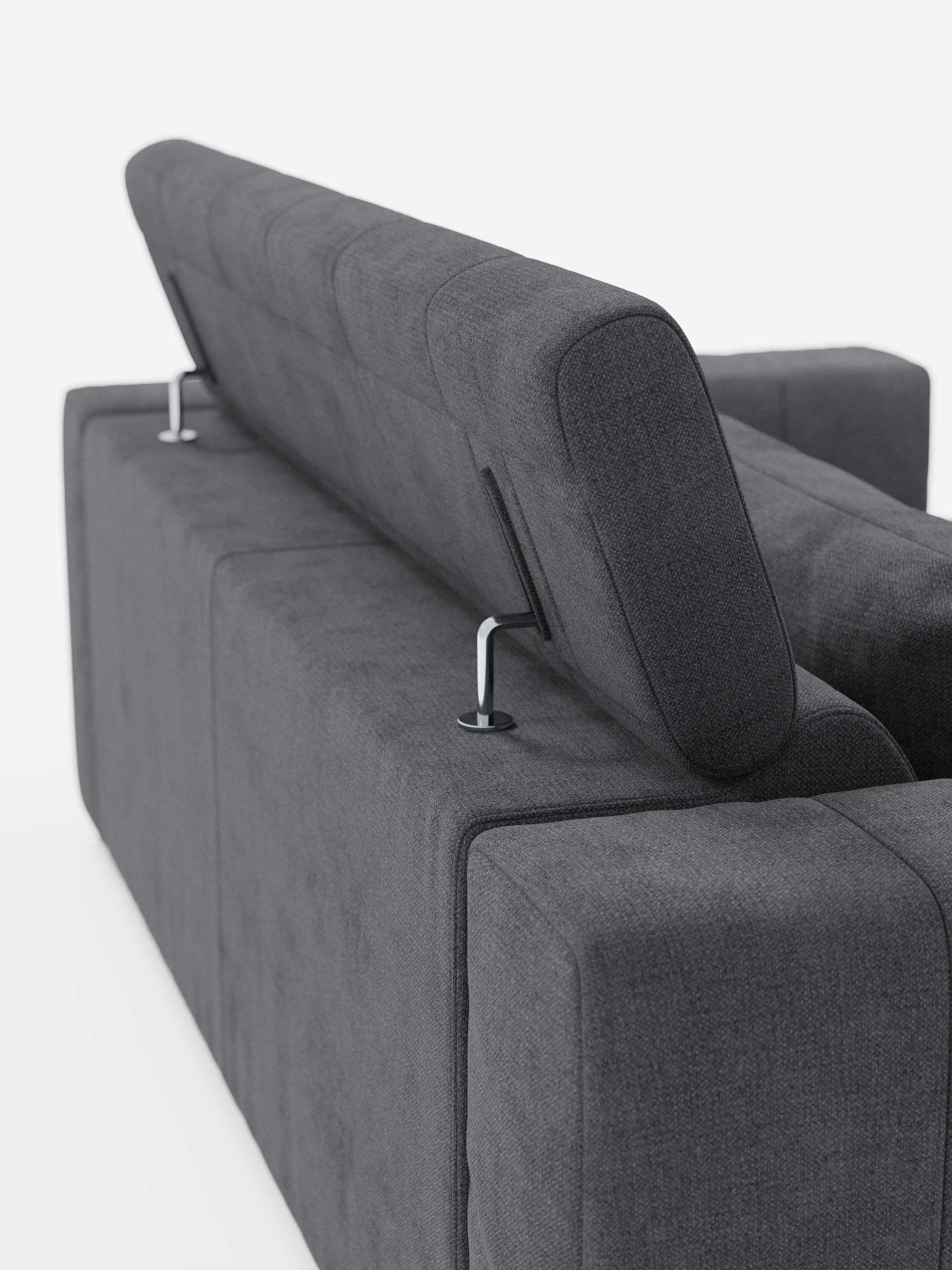 Un primo piano del divano a 3 posti Doric di Divani.Store, in grigio scuro, mostra un poggiatesta regolabile sollevato e l’altro in posizione orizzontale. Il tessuto sfoderabile T23 presenta una trama in rilievo, mentre lo sfondo bianco a tinta unita mette in risalto le linee slanciate del divano e i supporti metallici dei poggiatesta; le sedute sono inoltre dotate di estensione elettrica relax per un comfort ancora maggiore.