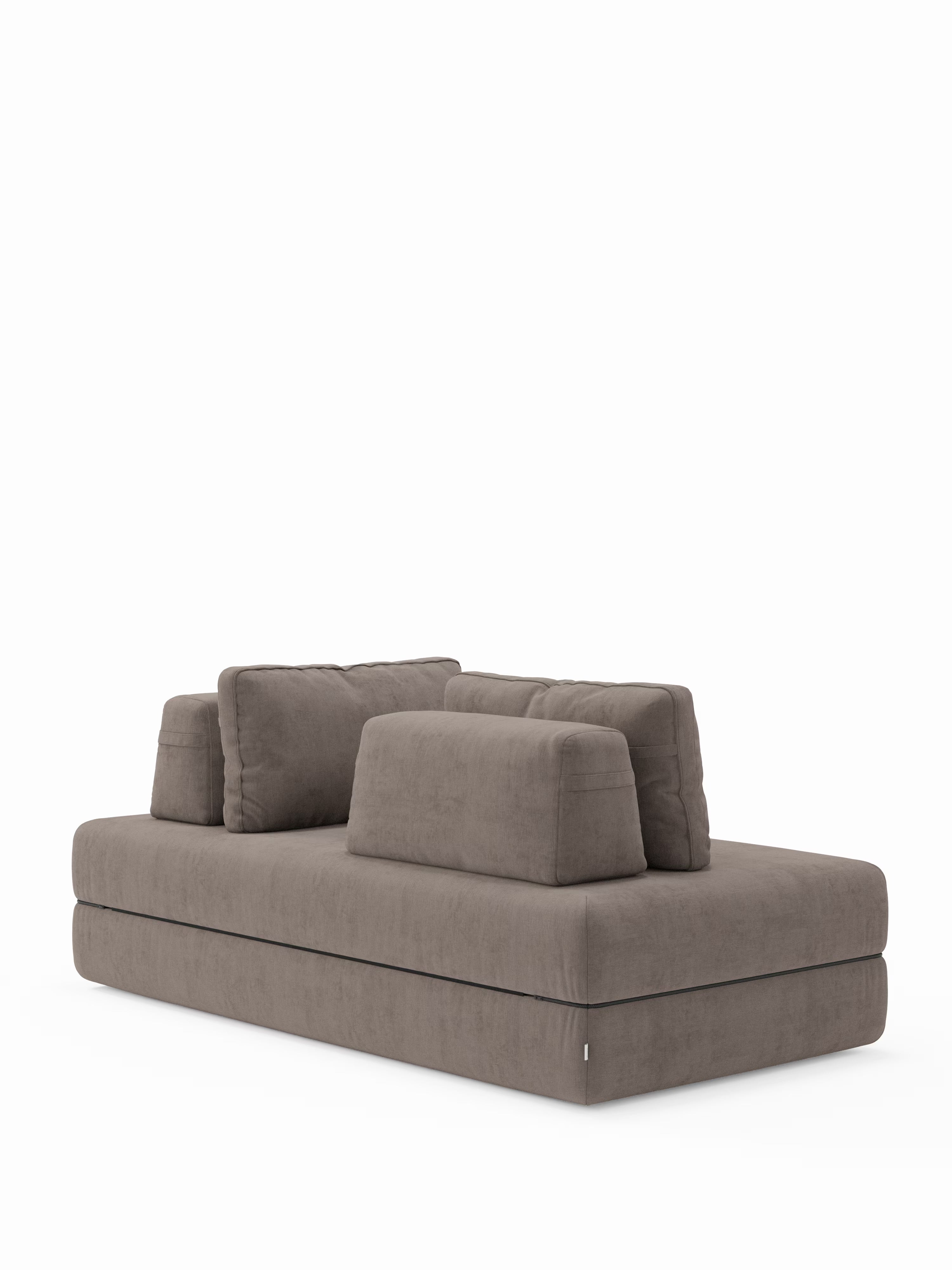 Un divano letto matrimoniale rettangolare in tessuto color taupe dal design contemporaneo, modello “Rift” a 2 e 3 posti con schienali mobili, di Divani.Store, caratterizzato da uno schienale basso con due cuscini grandi e due piccoli coordinati. Questo divano letto trasformabile è rivestito in tessuto T31 con un materasso in memory foam alto 22 cm ed è poggiato su una base piatta senza gambe a vista, presentato su uno sfondo bianco a tinta unita.