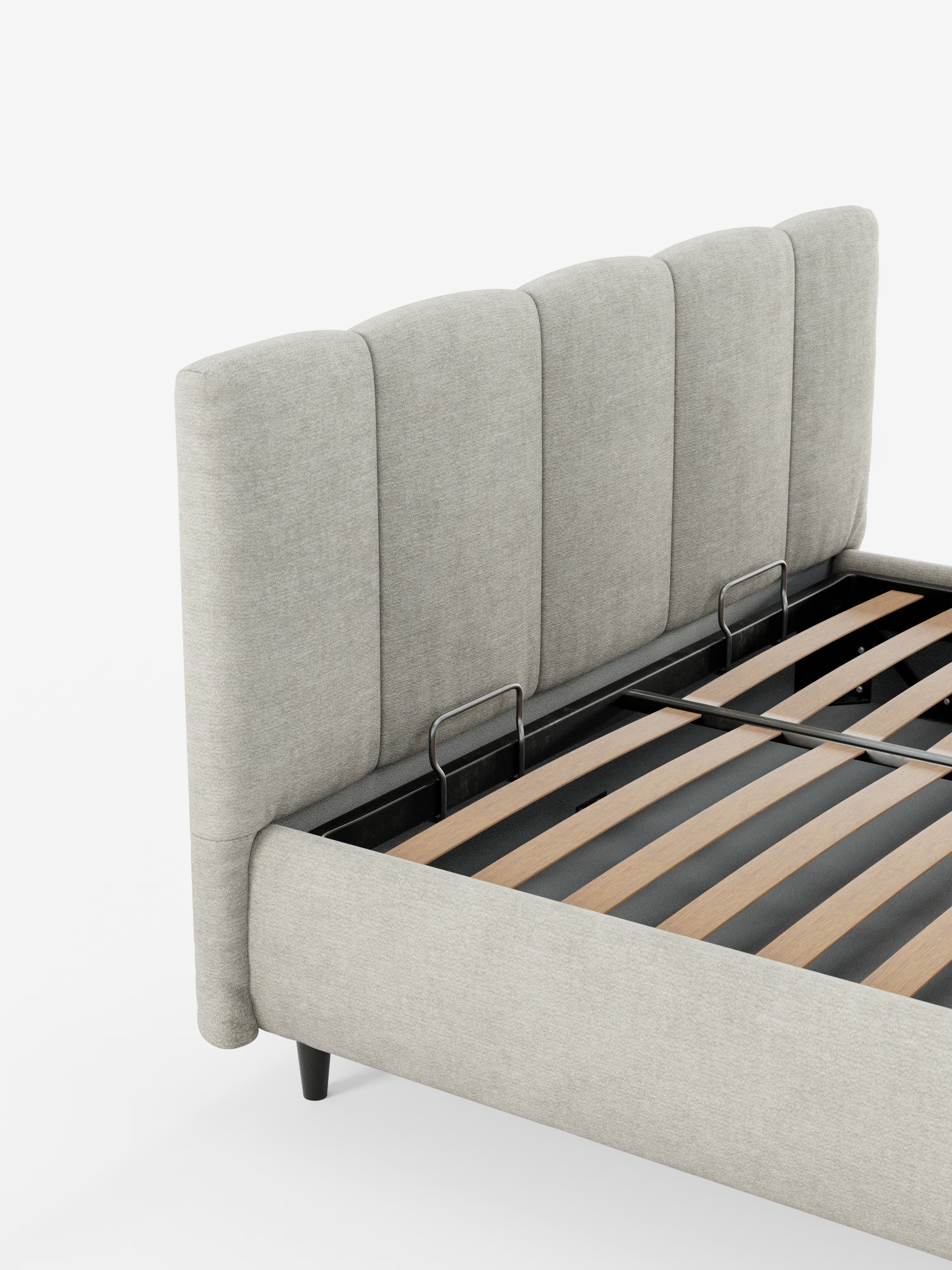 Un primo piano del letto imbottito ARKAM con contenitore e testiera a lavorazione verticale di Letti.store ne mette in risalto il design moderno in stile shabby chic, caratterizzato da una testiera alta, con pannelli verticali, di colore grigio chiaro, rivestita in tessuto certificato Oeko-Tex®. La struttura del letto è sostenuta da gambe affusolate di colore nero e presenta doghe in legno parzialmente visibili, il tutto su uno sfondo bianco a tinta unita.