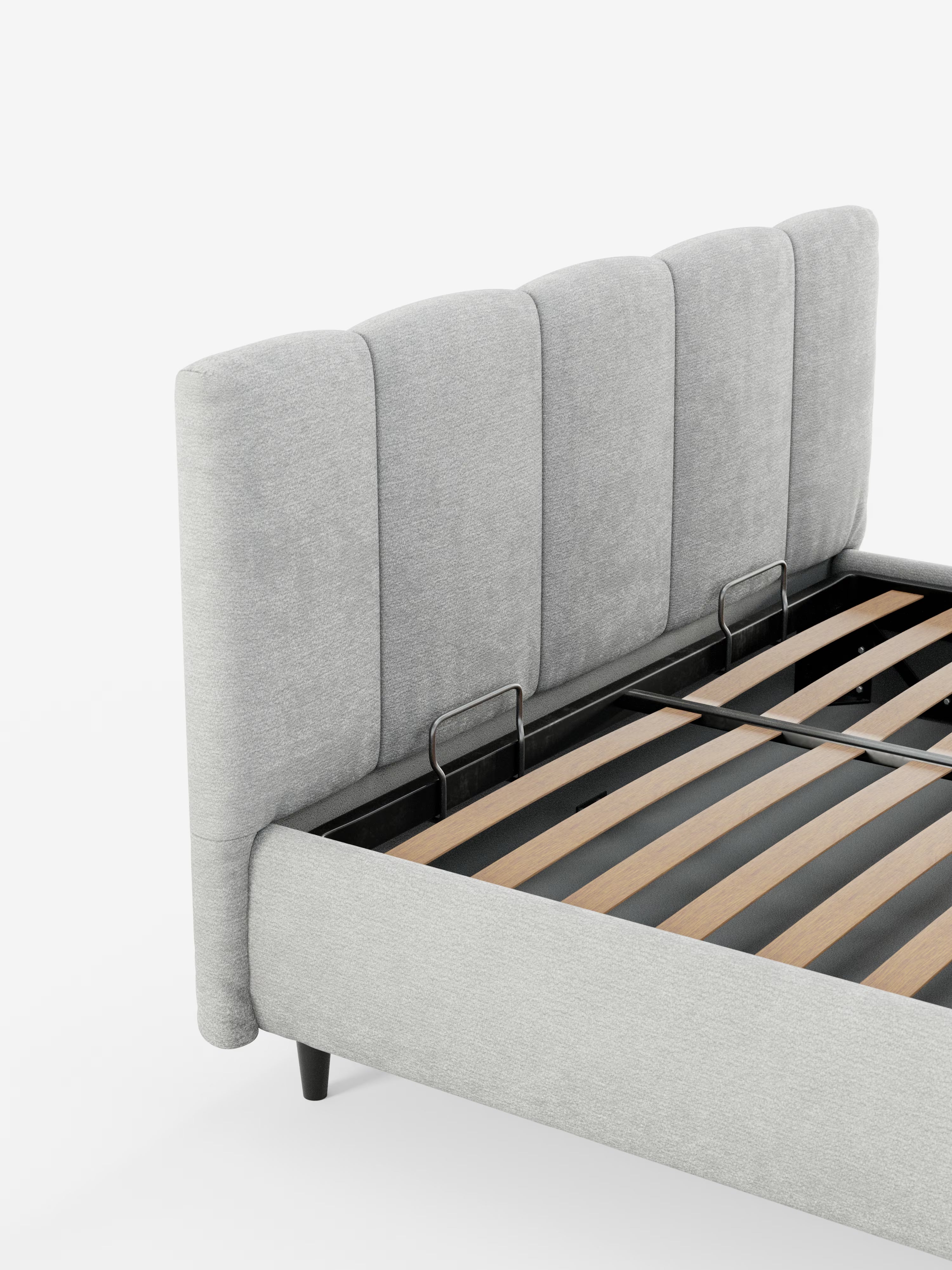Il letto imbottito ARKAM con contenitore e testiera a lavorazione verticale di Letti.store è rivestito in tessuto grigio chiaro certificato Oeko-Tex® e presenta un design shabby chic. Questo letto imbottito è dotato di una testiera alta e imbottita con canalature verticali, doghe in legno con una robusta struttura in metallo nero e gambe corte nere. L’immagine mostra il letto parzialmente in primo piano su uno sfondo bianco a tinta unita.
