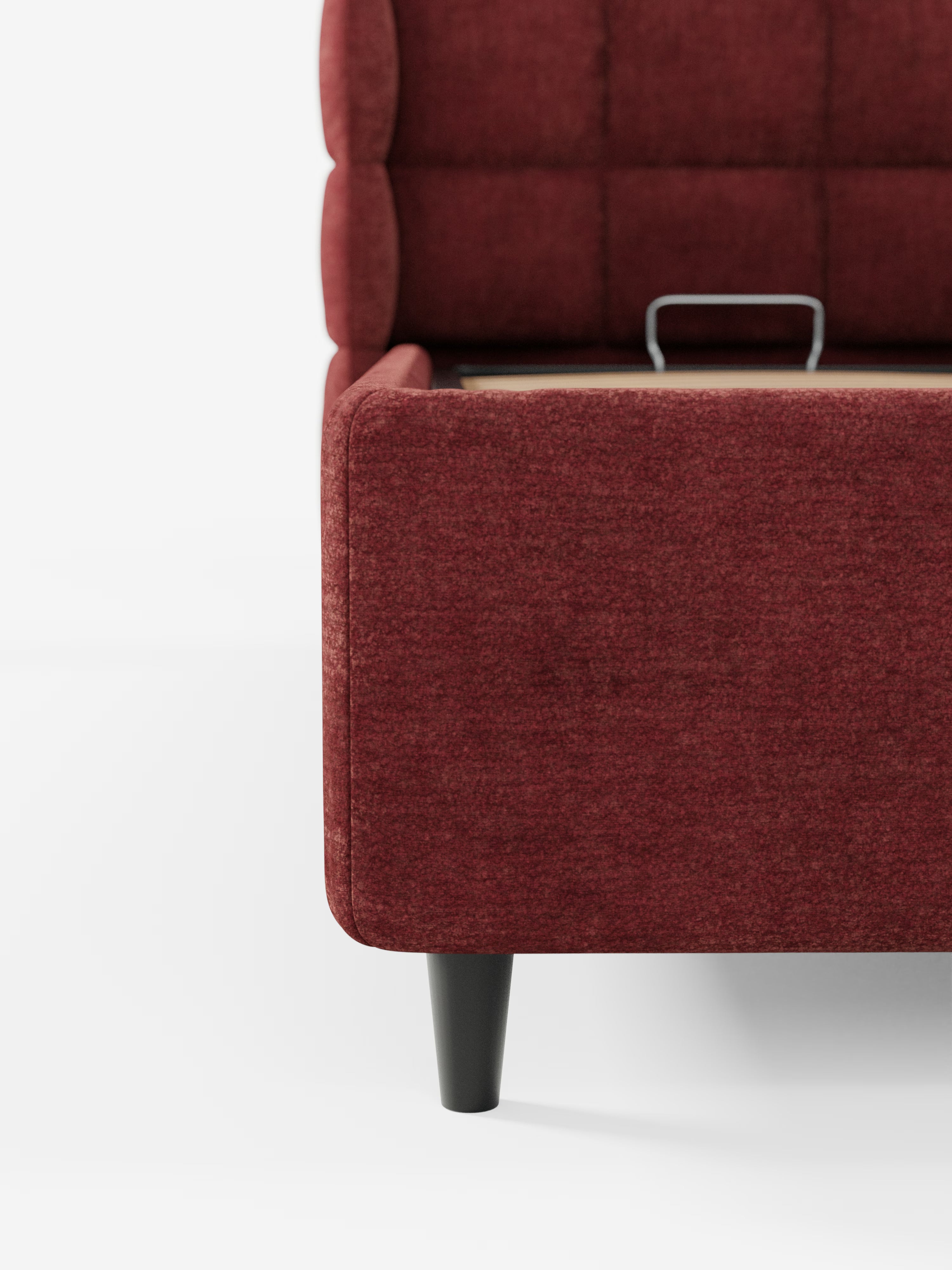 Primo piano della pediera e del pannello laterale del letto imbottito RAGNAR con vano contenitore e testiera capitonné avvolgente di Letti.store, rivestito in tessuto marrone certificato Oeko-Tex®, con gambe affusolate nere. Un vano contenitore aperto con maniglia in metallo sottolinea il carattere pratico di questo elegante letto contenitore. Immagine su sfondo bianco.