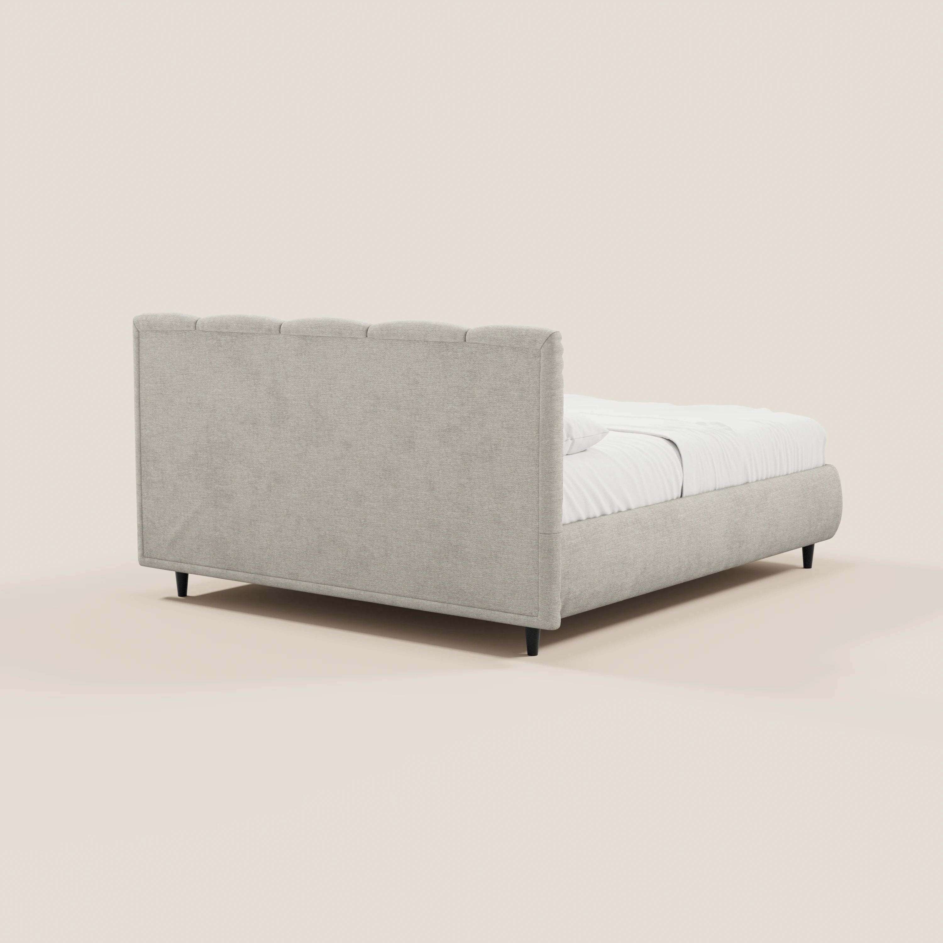 Il letto imbottito ARKAM di Letti.store presenta una testiera alta con cuciture verticali e una pediera abbinata in tessuto certificato Oeko-Tex®, in stile shabby chic, su gambe corte nere con biancheria da letto bianca. Lo sfondo è di colore crema chiaro a tinta unita.